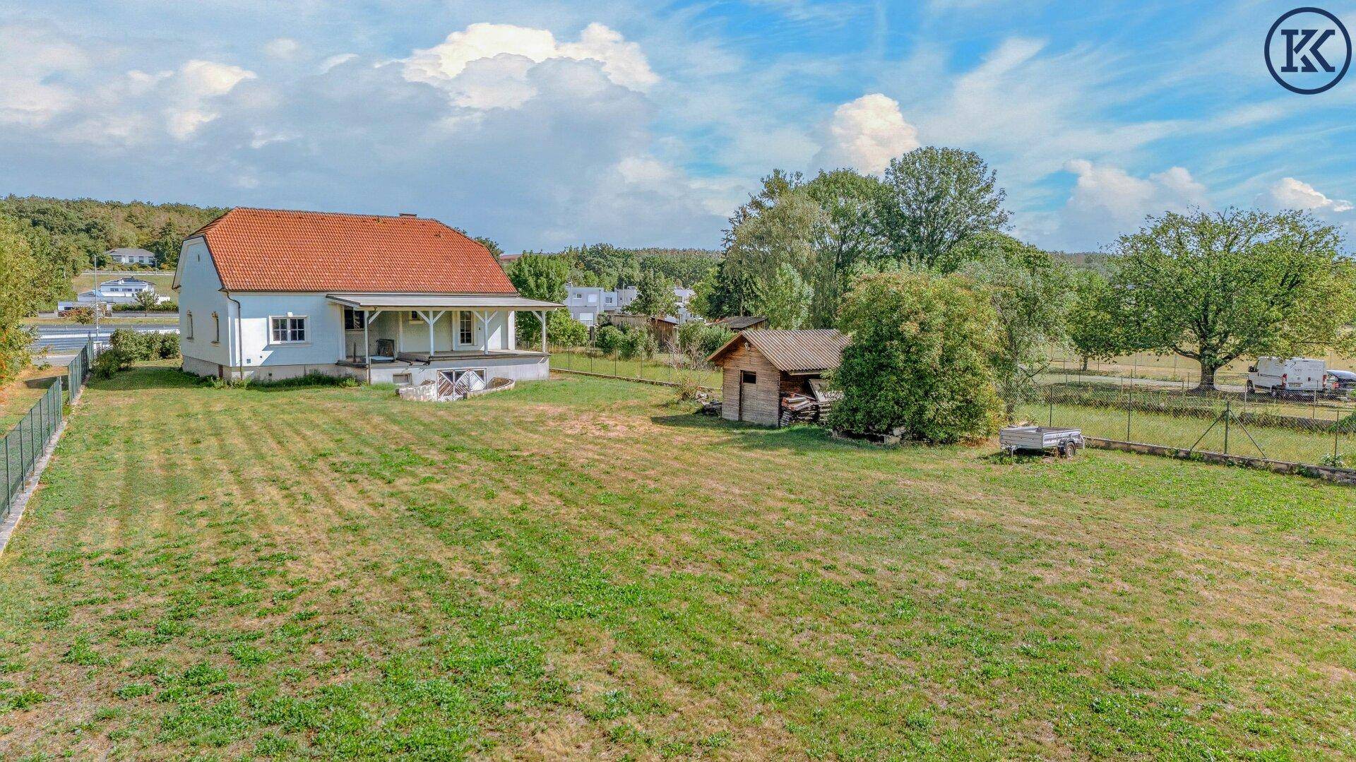 Gesamtansicht des Anwesens mit Haus, großem Garten und einem Holzschuppen unter blauem Himmel.