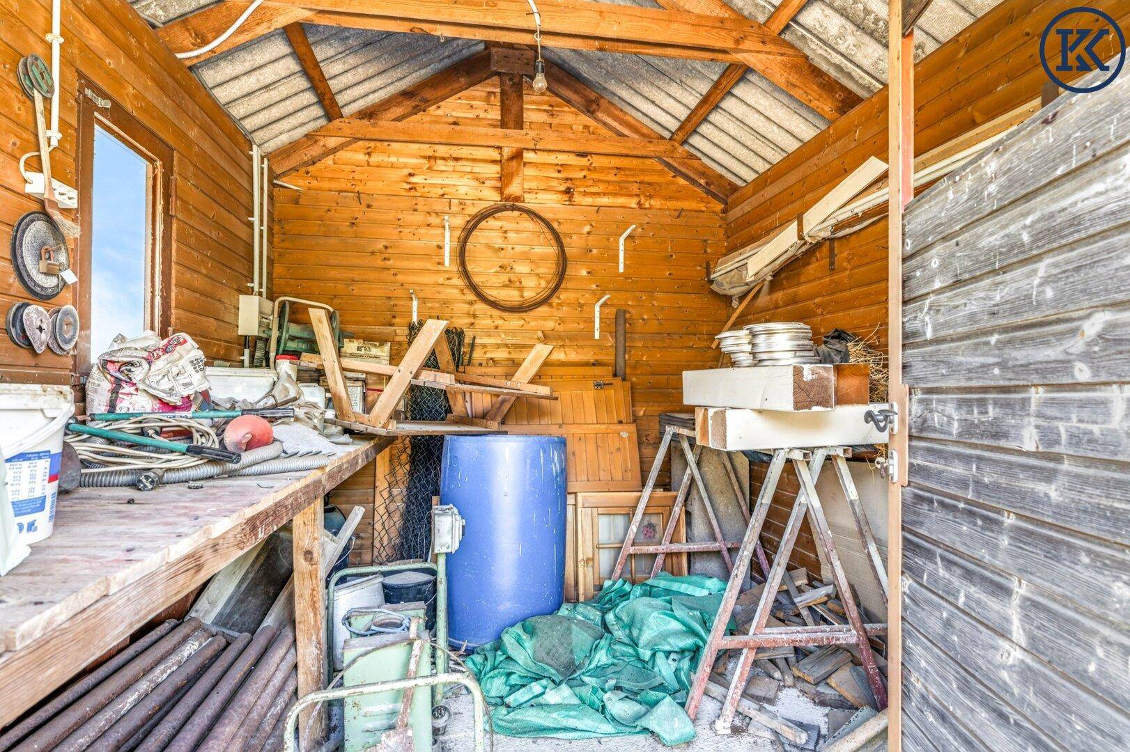 Innenansicht des Holzschuppens mit sichtbarer Holzkonstruktion und gelagerten Gegenständen, rustikaler Charme.