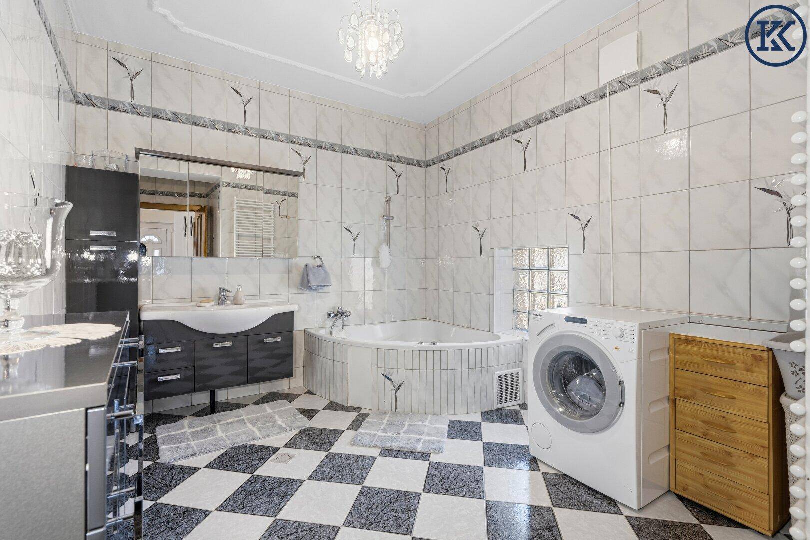 Geräumiges Badezimmer mit Eckbadewanne, Waschmaschine und schwarz-weißem Fliesenboden.