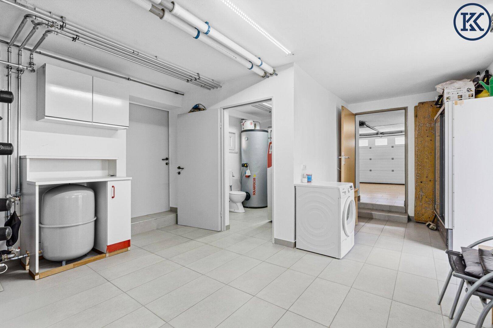 Waschküche im Keller mit Waschmaschine, Schränken und Zugang zum Heizungsraum.