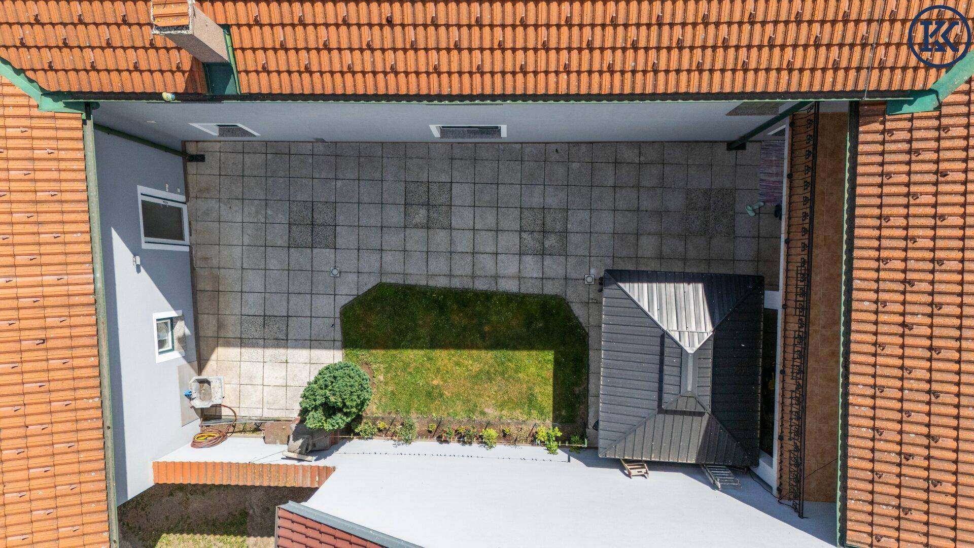 Luftaufnahme des Innenhofs mit gepflasterter Fläche, Rasen und Gartenlaube.