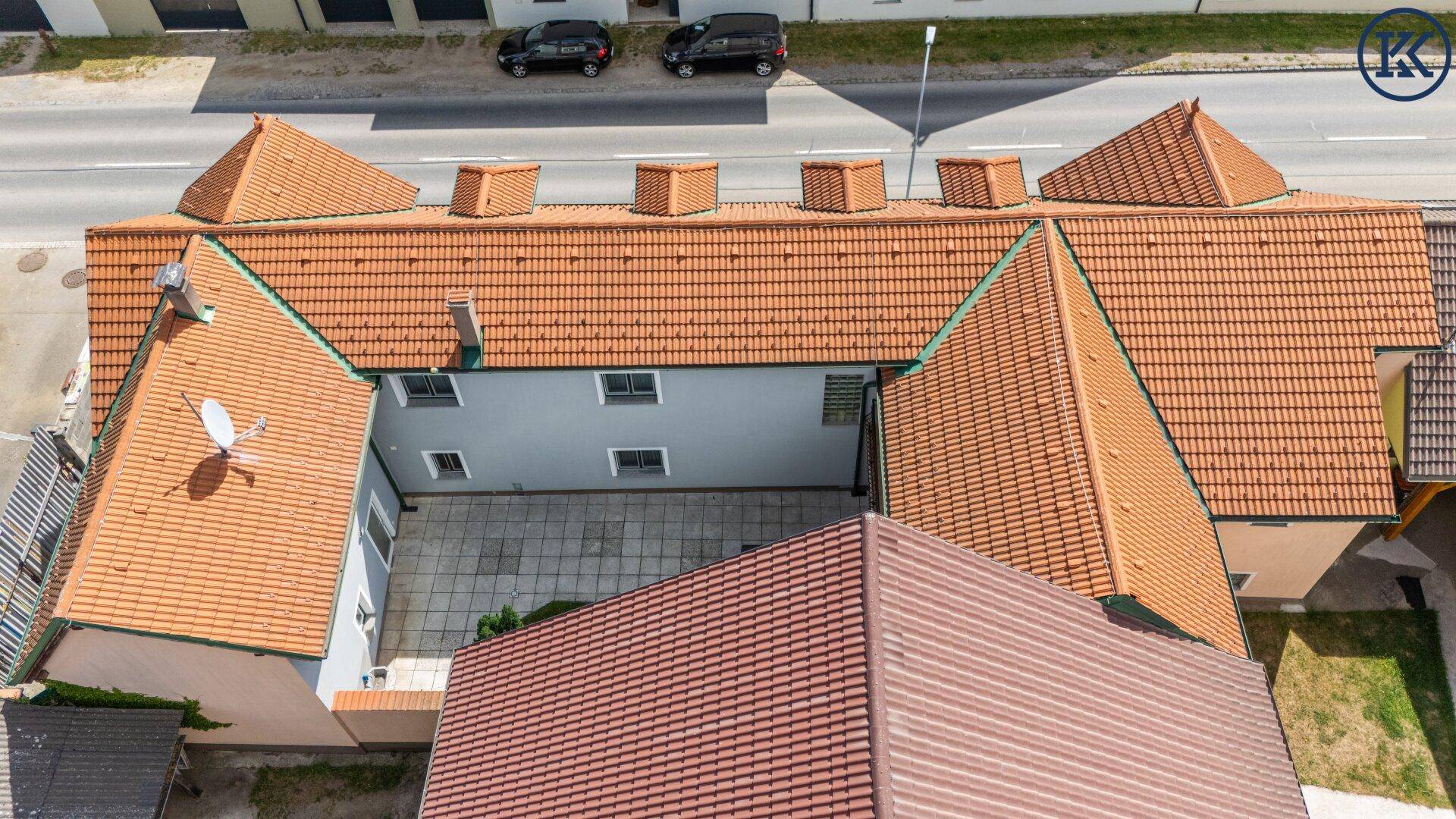 Luftaufnahme des Gebäudekomplexes mit Dächern, Innenhof und angrenzender Straße.