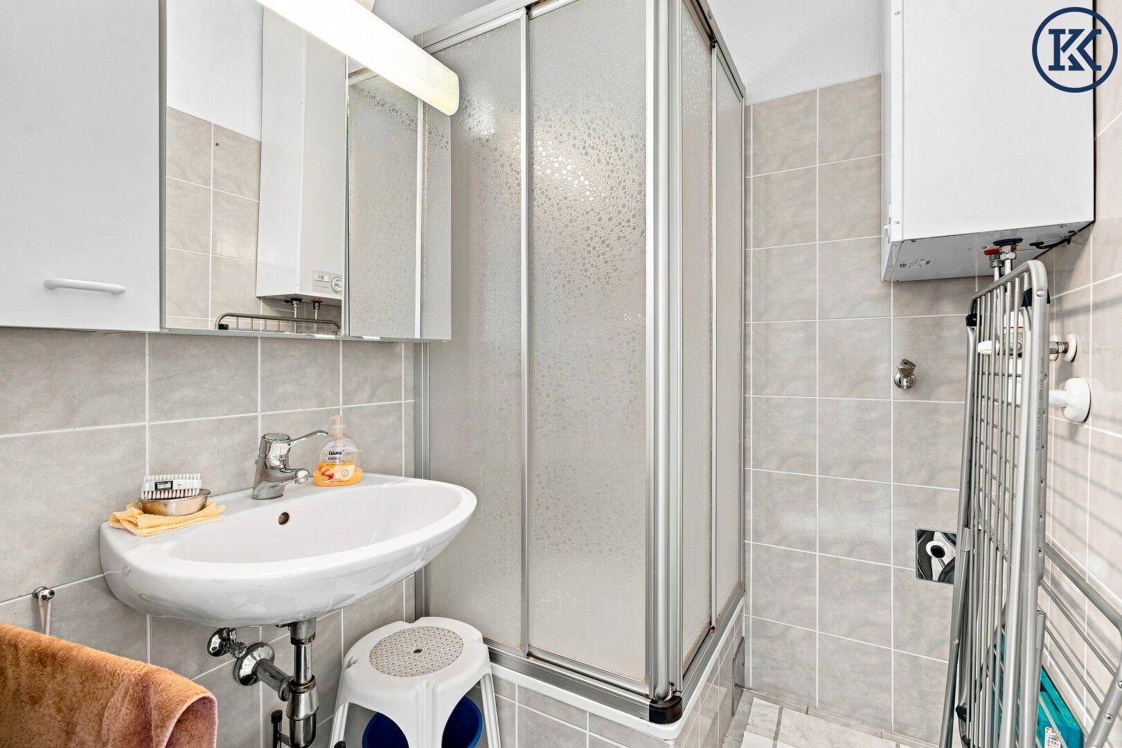 Kleines Badezimmer mit Dusche, Waschbecken und grauen Fliesen an den Wänden.