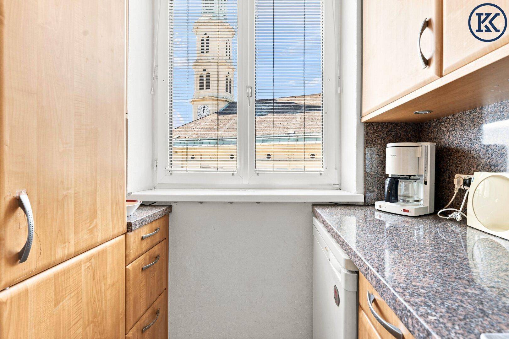 Küchenfenster mit Blick auf einen Kirchturm, umgeben von hellen Holzschränken und Granitarbeitsplatten.