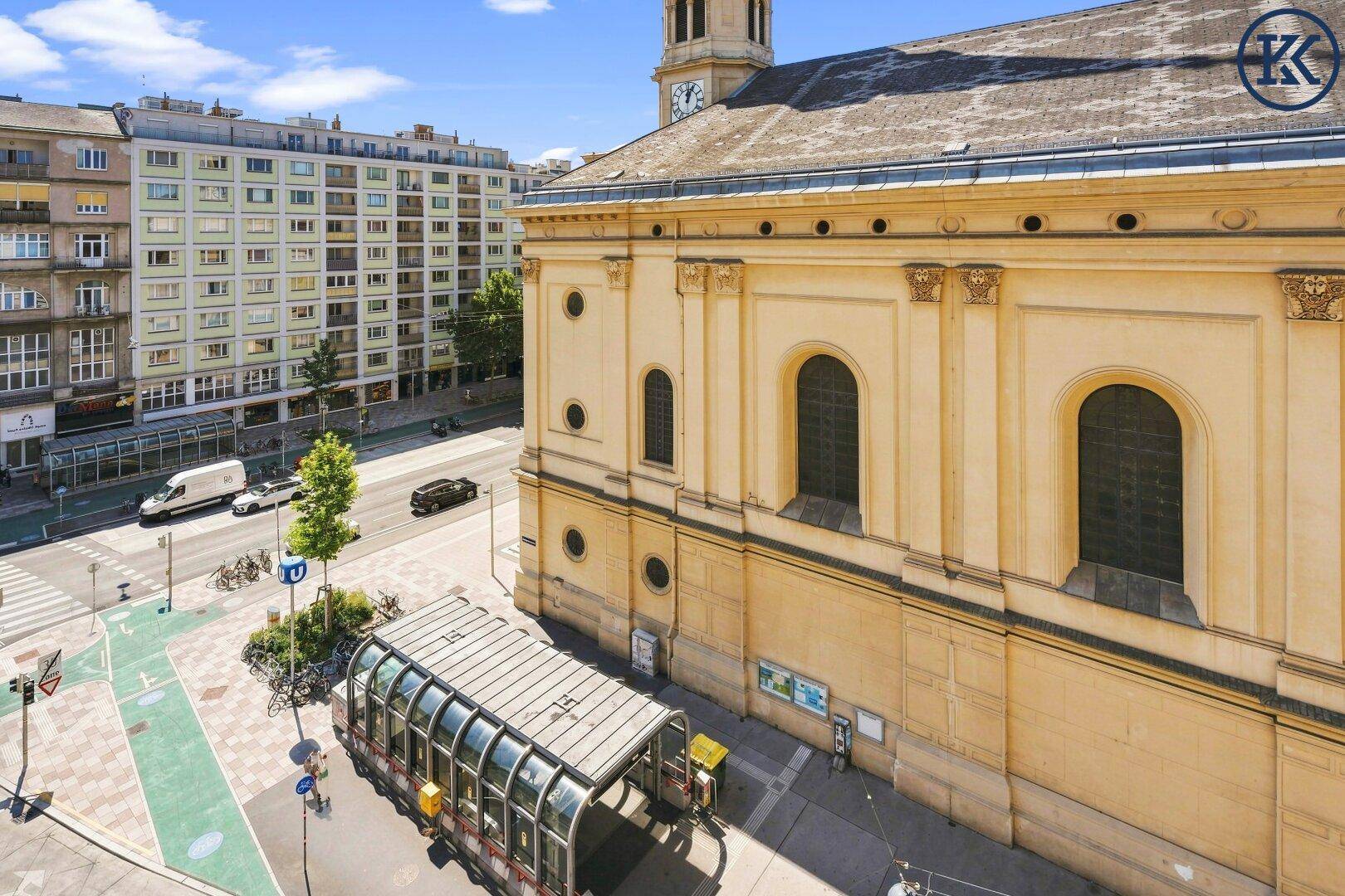 Luftaufnahme einer Kirche und umliegender Gebäude mit einer U-Bahn-Station im Vordergrund.