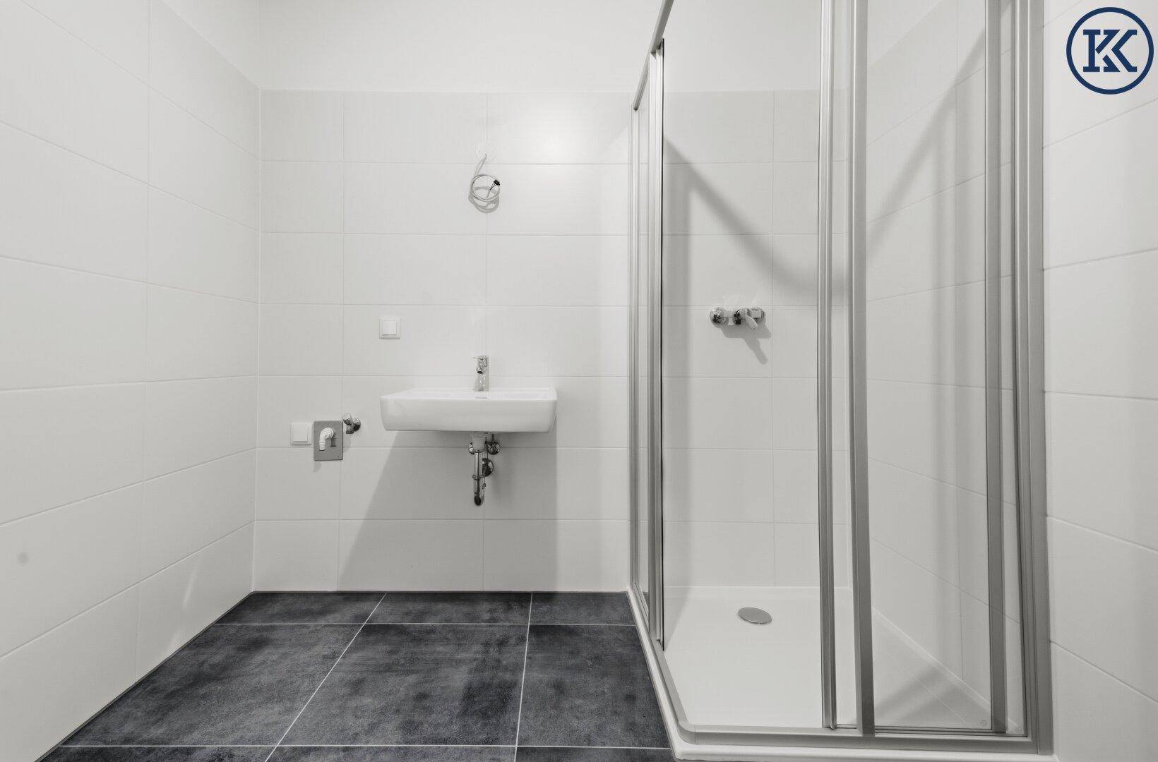Modernes Badezimmer mit weißen Wandfliesen, dunklem Boden und einer praktischen Duschkabine.