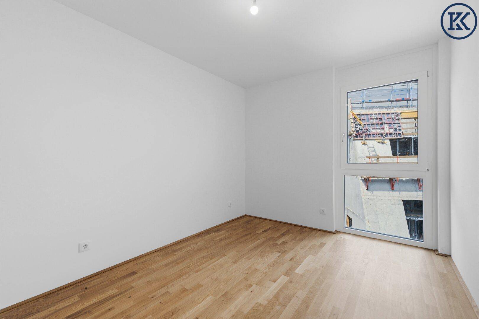 Helles Schlafzimmer mit Parkettboden und Fenster, das viel Tageslicht hereinlässt.