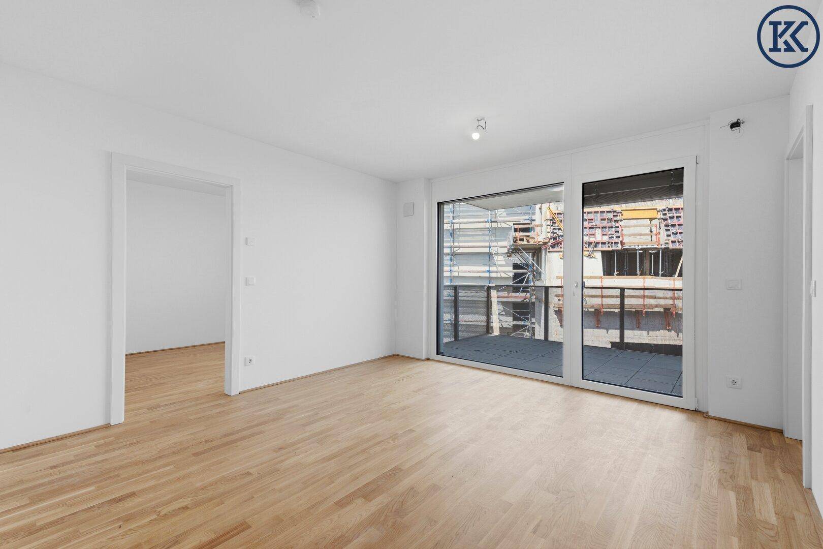 Helles Wohnzimmer mit Parkettboden und großen Fenstern, die auf einen Balkon führen.