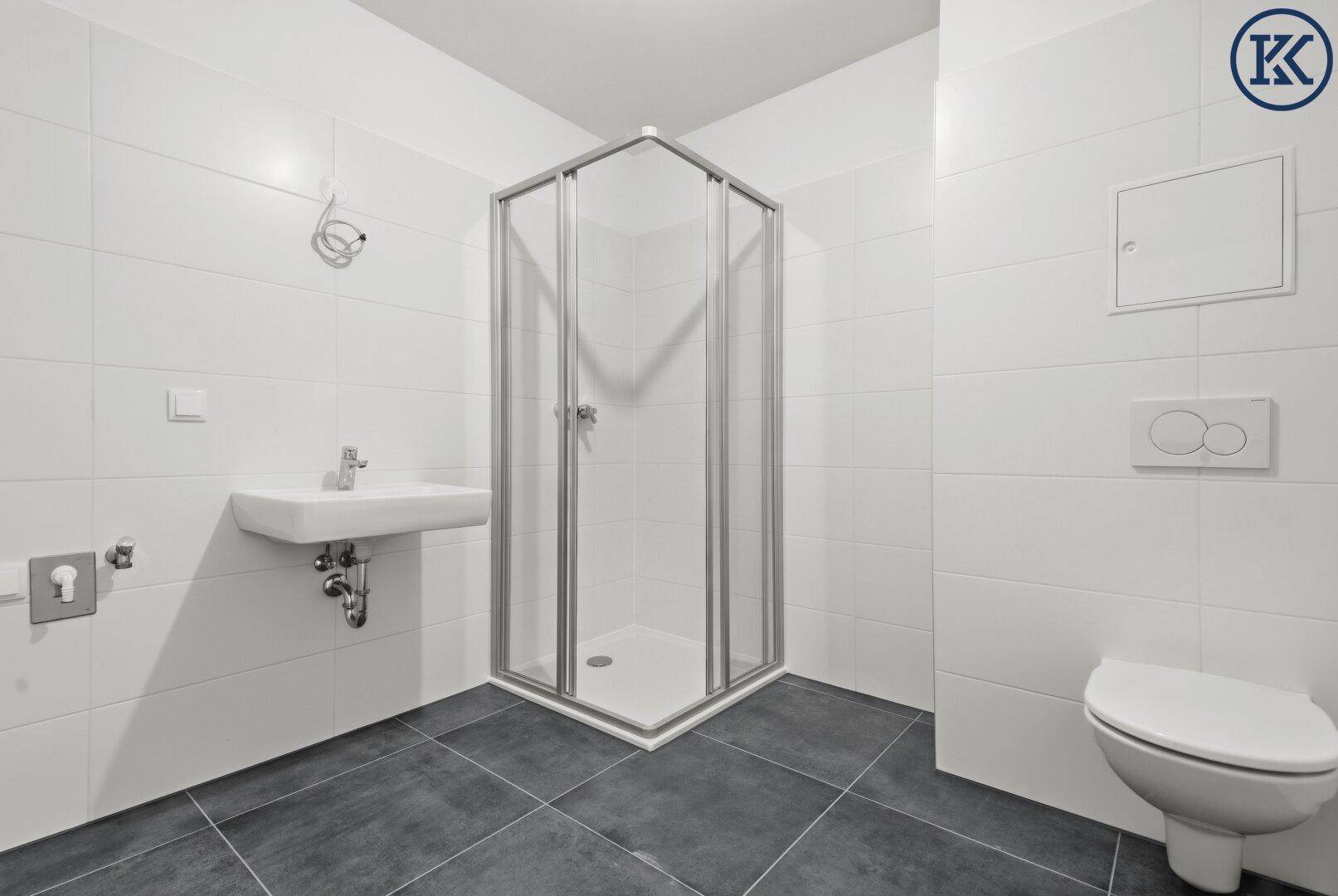 Modernes Badezimmer mit weißen Wandfliesen, dunklem Boden und einer Duschkabine.