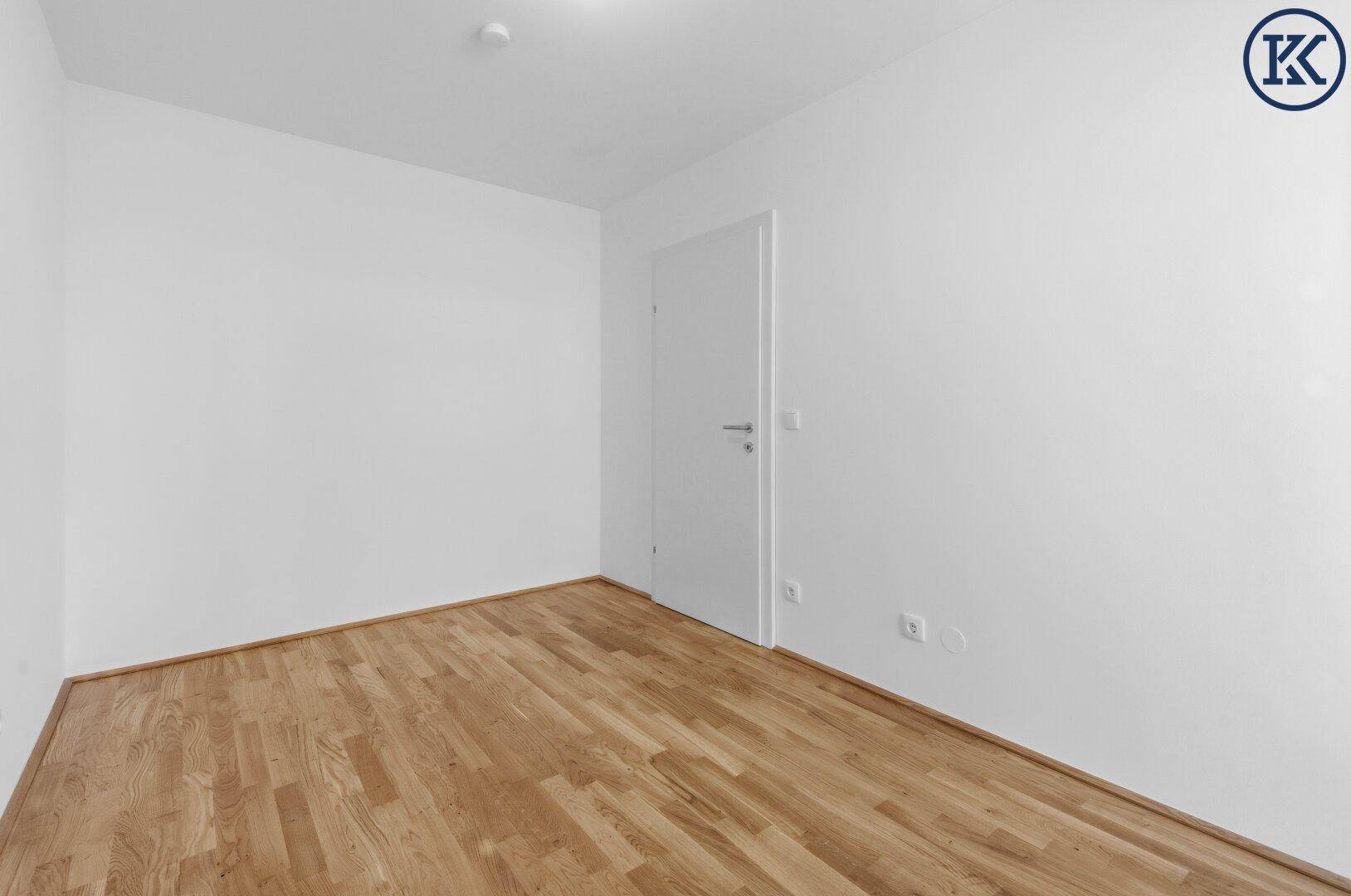 Leeres Zimmer mit hellem Parkettboden und weißer Tür, bereit zur individuellen Gestaltung.