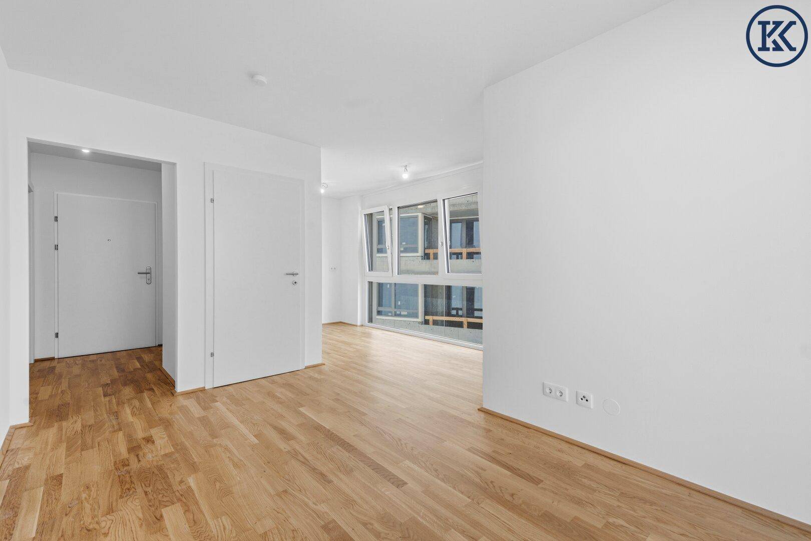 Geräumiger, heller Raum mit Parkettboden und großen Fenstern, die viel Licht hereinlassen.