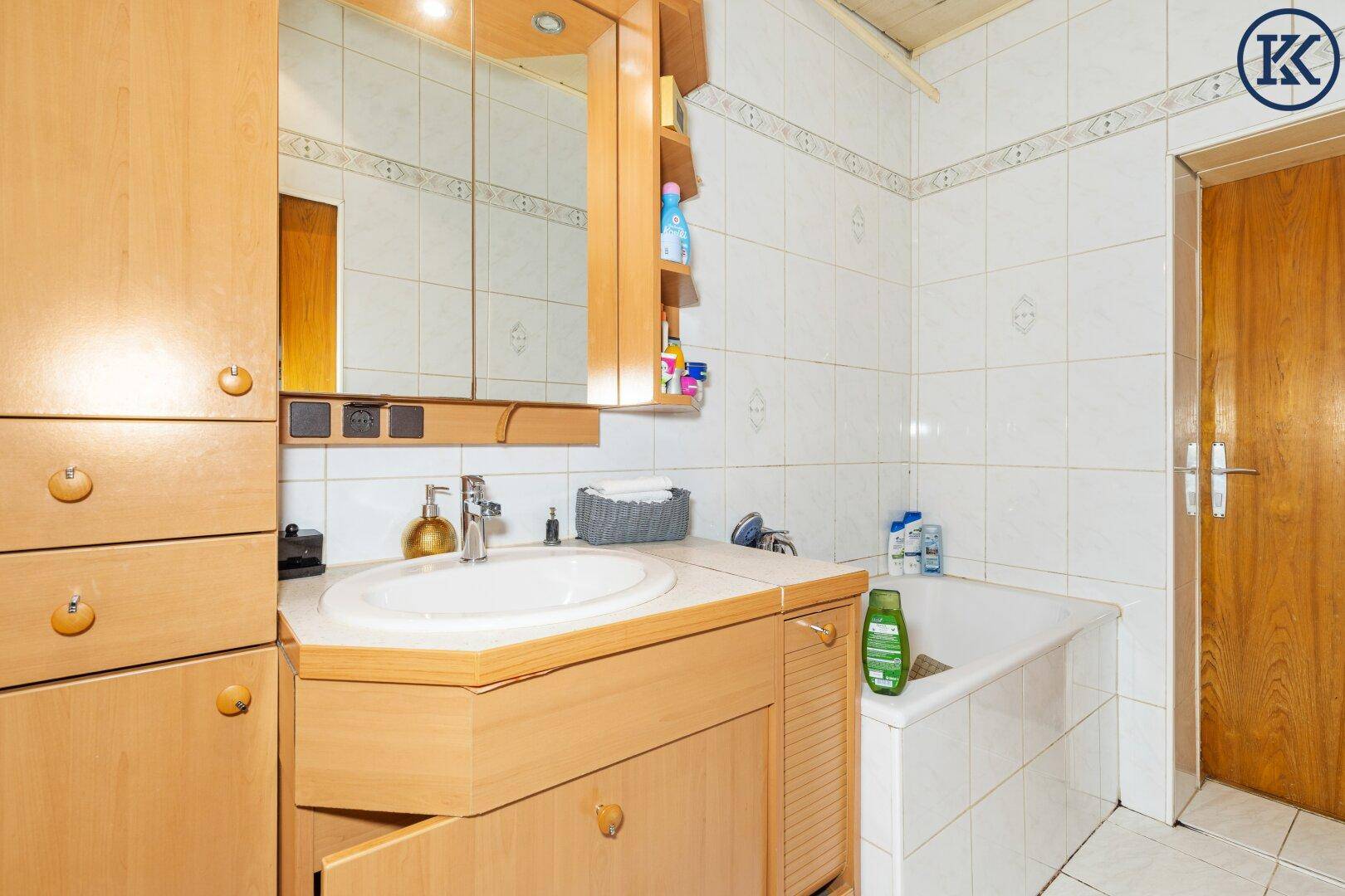 Badezimmer mit Badewanne, Waschbecken und Holzschränken, komplett gefliest.