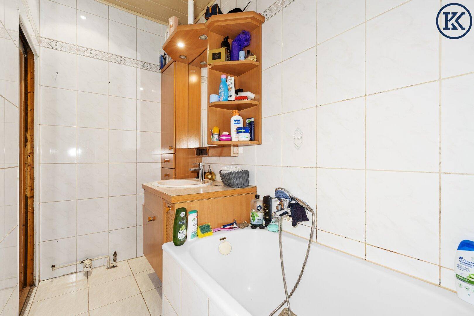 Badezimmer mit Badewanne, Waschbecken und Spiegelschrank, hell gefliest.