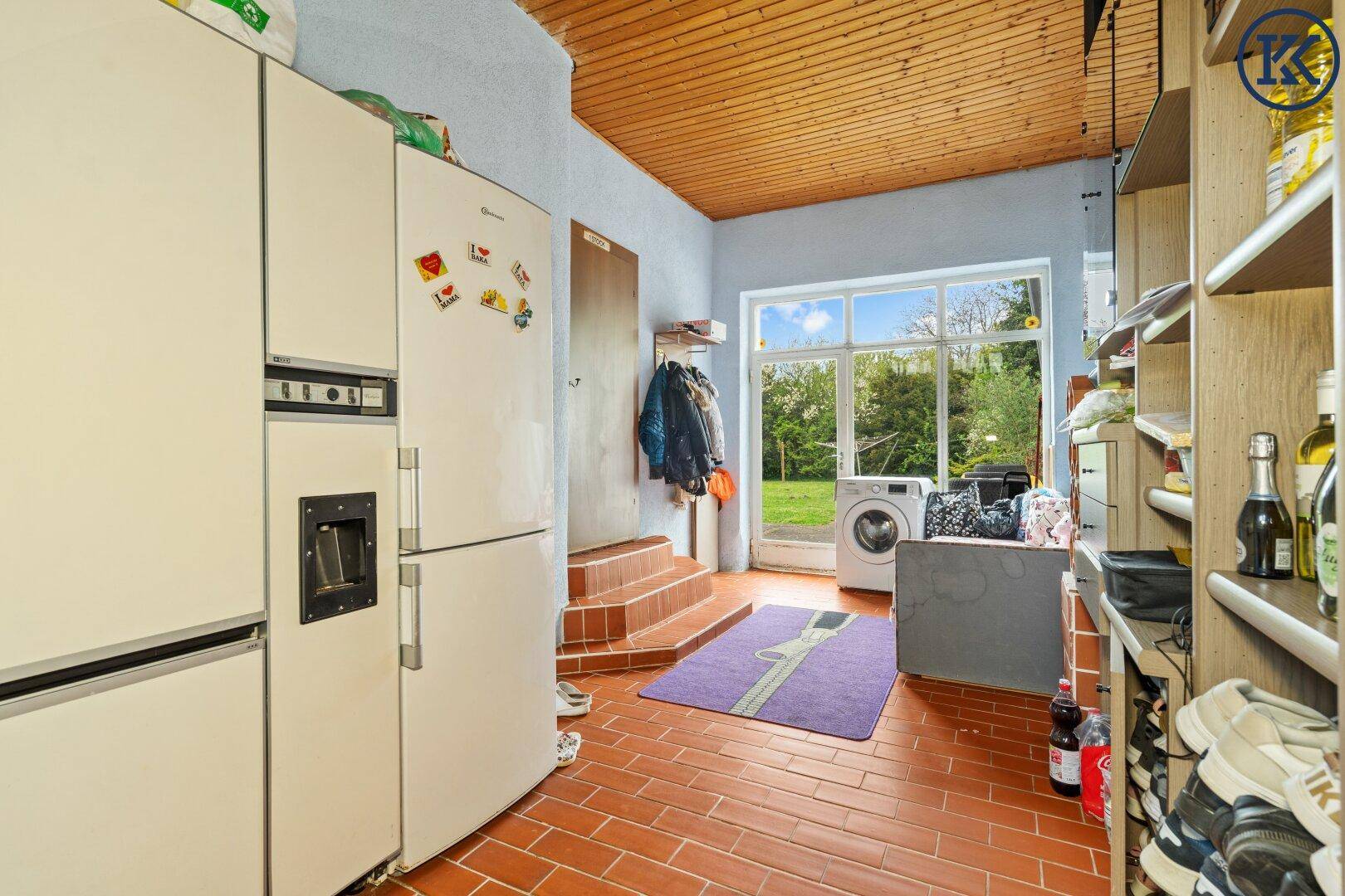Praktischer Hauswirtschaftsraum mit Waschmaschine, Kühlschränken und Zugang zum Garten.