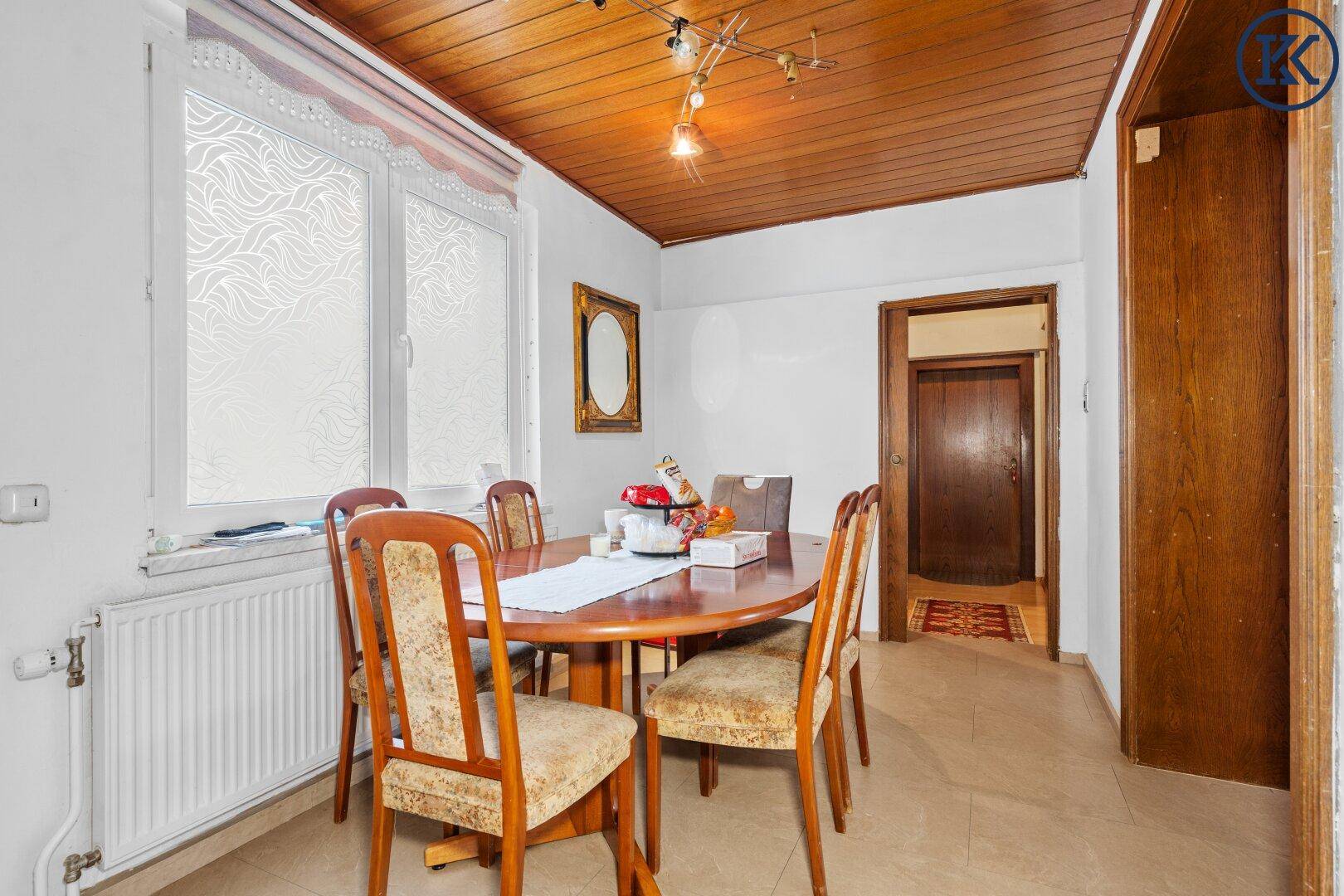 Gemütliches Esszimmer mit ovalem Holztisch, Stühlen und einem Fenster mit Heizkörper.