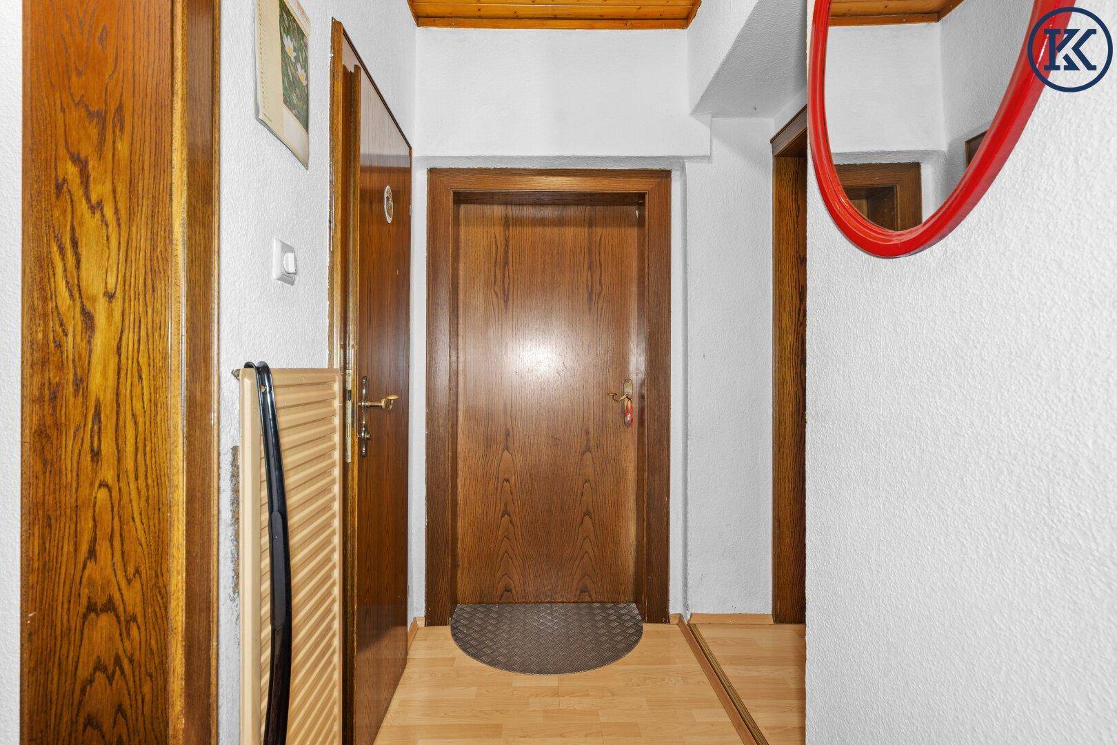 Schmaler Flur mit Holztüren, Parkettboden und einem Spiegel an der Wand.