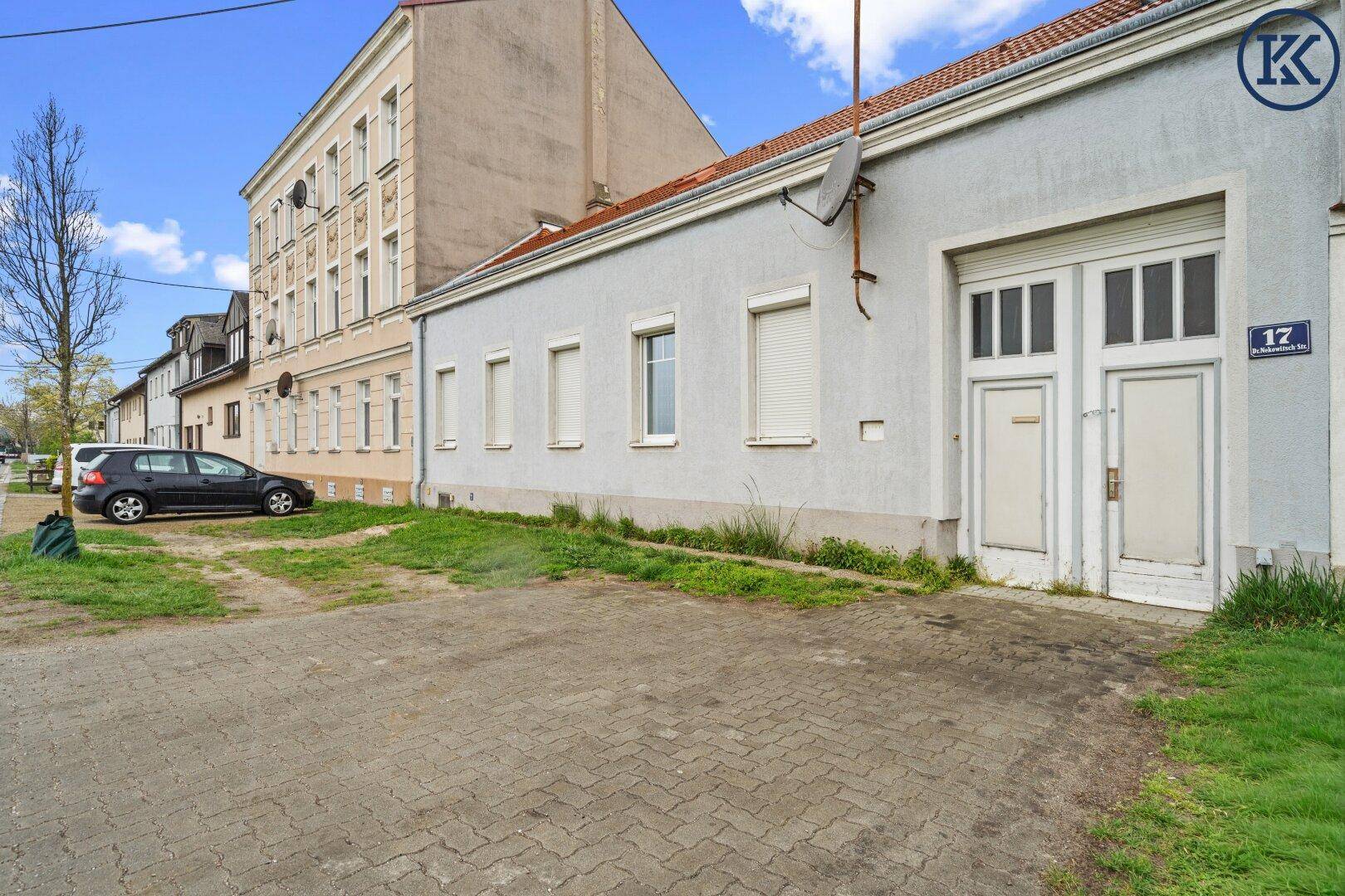 Rückseite eines Gebäudes mit gepflastertem Bereich und Garagentoren, angrenzend an ein Mehrfamilienhaus.