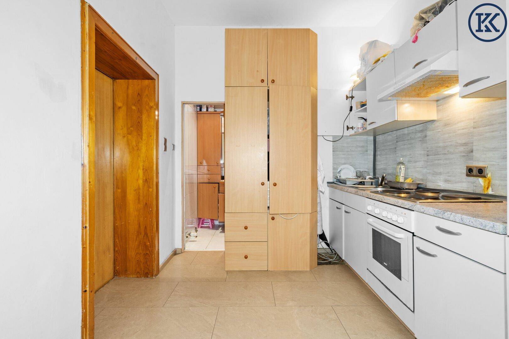 Einfache Küche mit weißen Unterschränken, Holzschrank und gefliestem Boden.