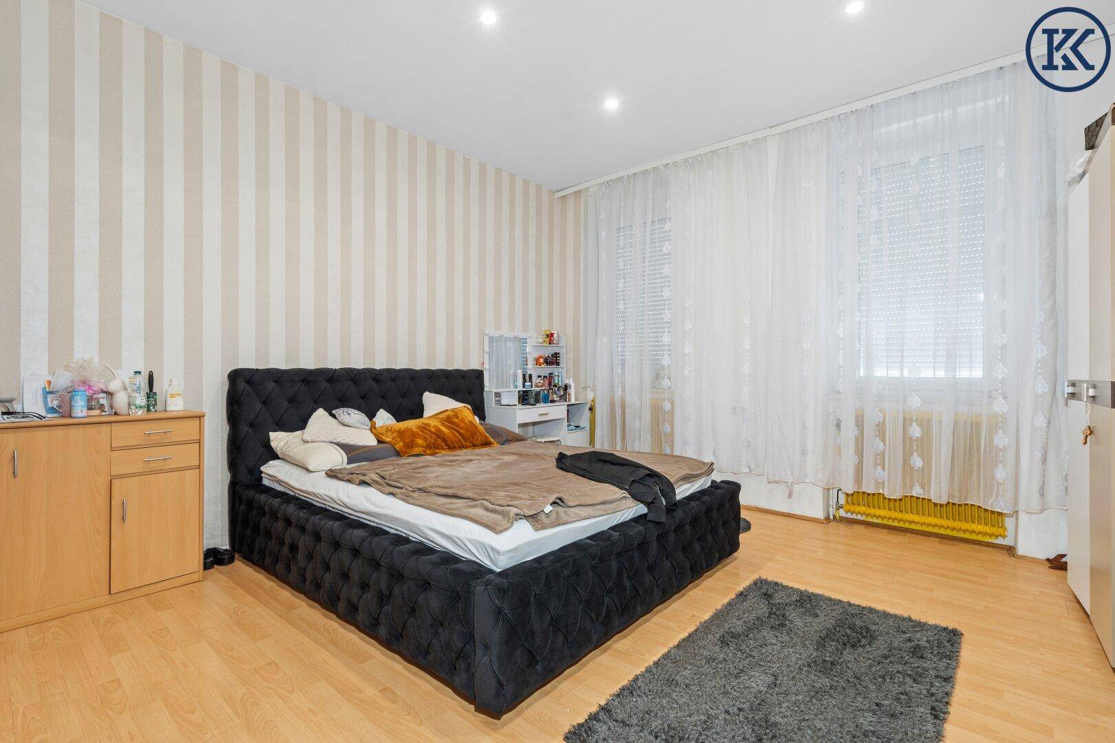 Schlafzimmer mit gestreifter Tapete, großem Bett und Holzfußboden.