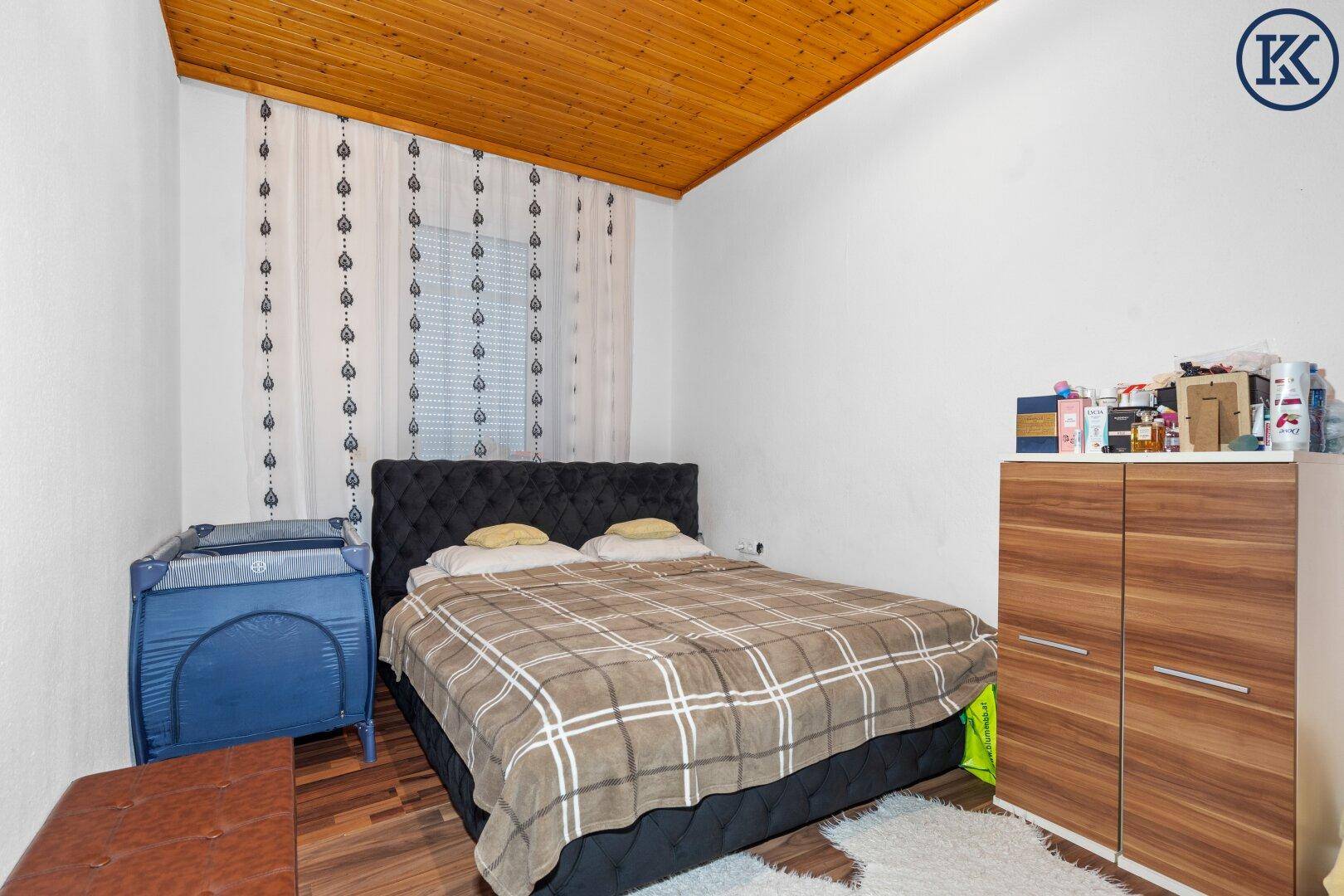 Schlafzimmer mit Doppelbett, Holzdecke und dunklem Laminatboden.