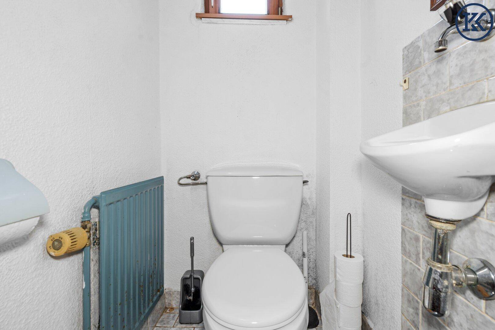 Kleines Gäste-WC mit Toilette, Waschbecken und Fenster.