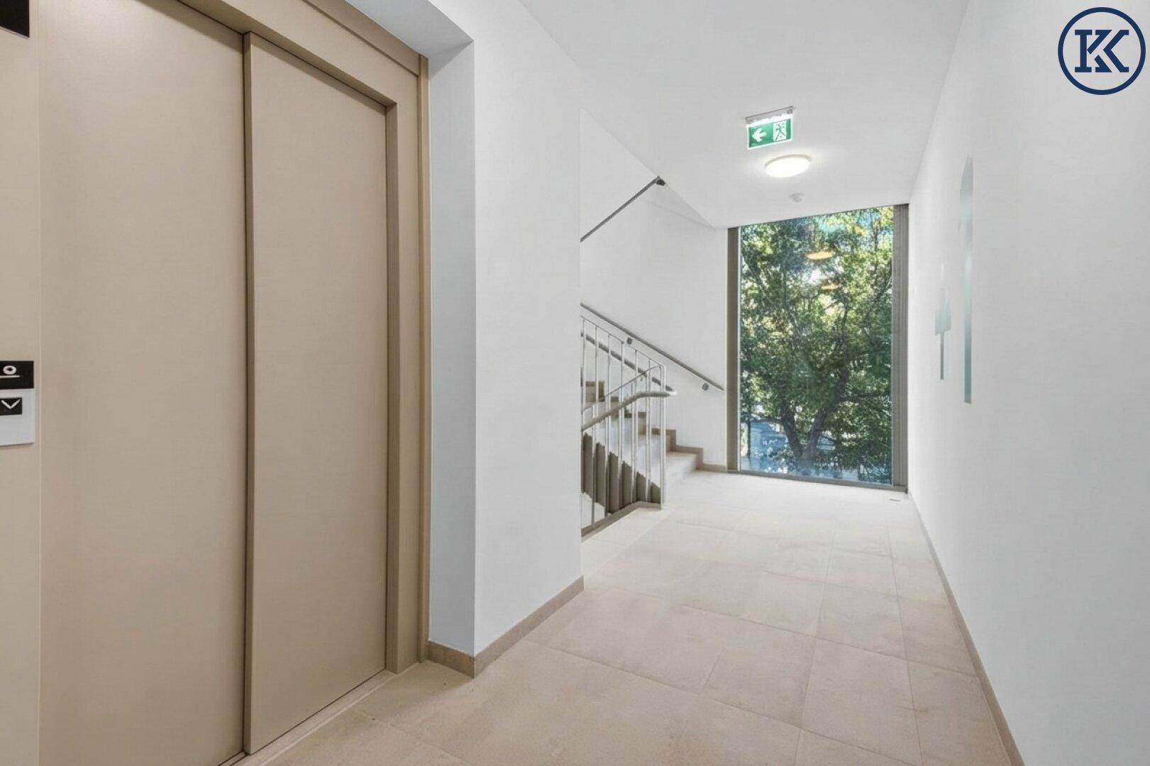Moderner Flur mit Aufzug und Treppenhaus, große Fenster bieten einen schönen Blick ins Grüne.