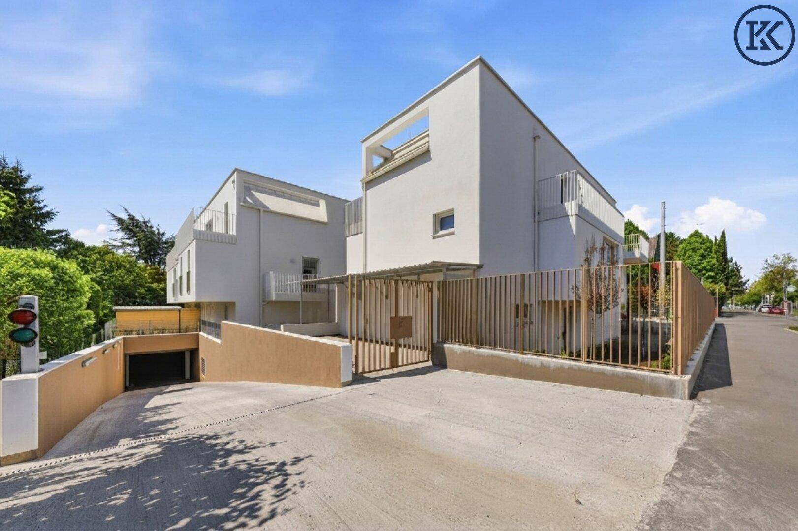 Moderne Wohngebäude mit weißer Fassade, Tiefgaragenzufahrt und umzäuntem Grundstück.