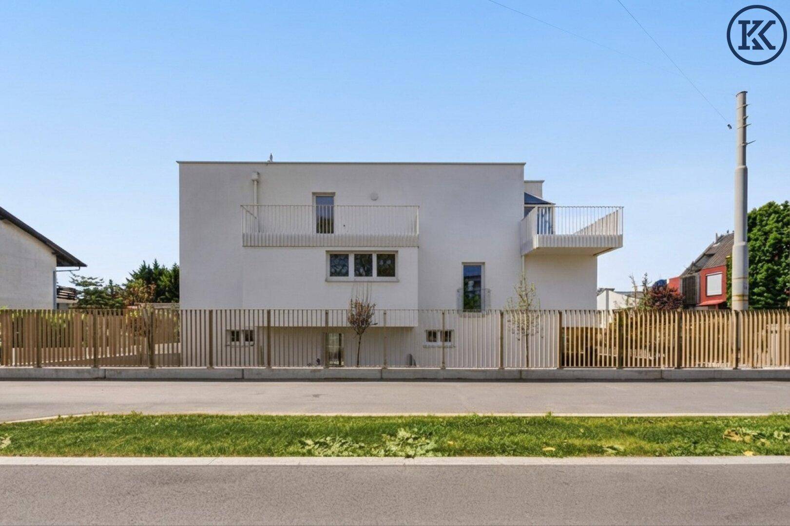 Moderne weiße Fassade eines Wohngebäudes mit Balkonen und Holzlattenzaun.