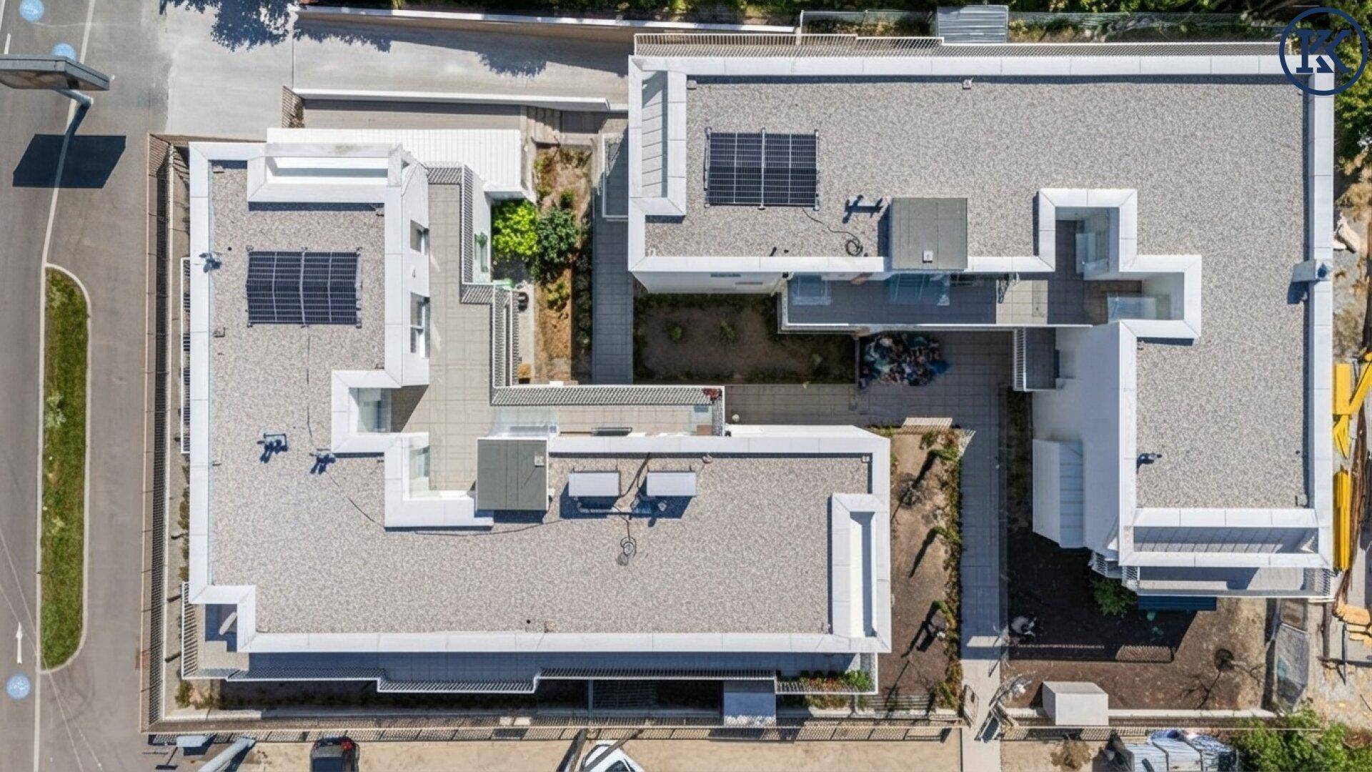 Draufsicht auf die Flachdächer der modernen Wohngebäude mit Solaranlagen und Innenhof.