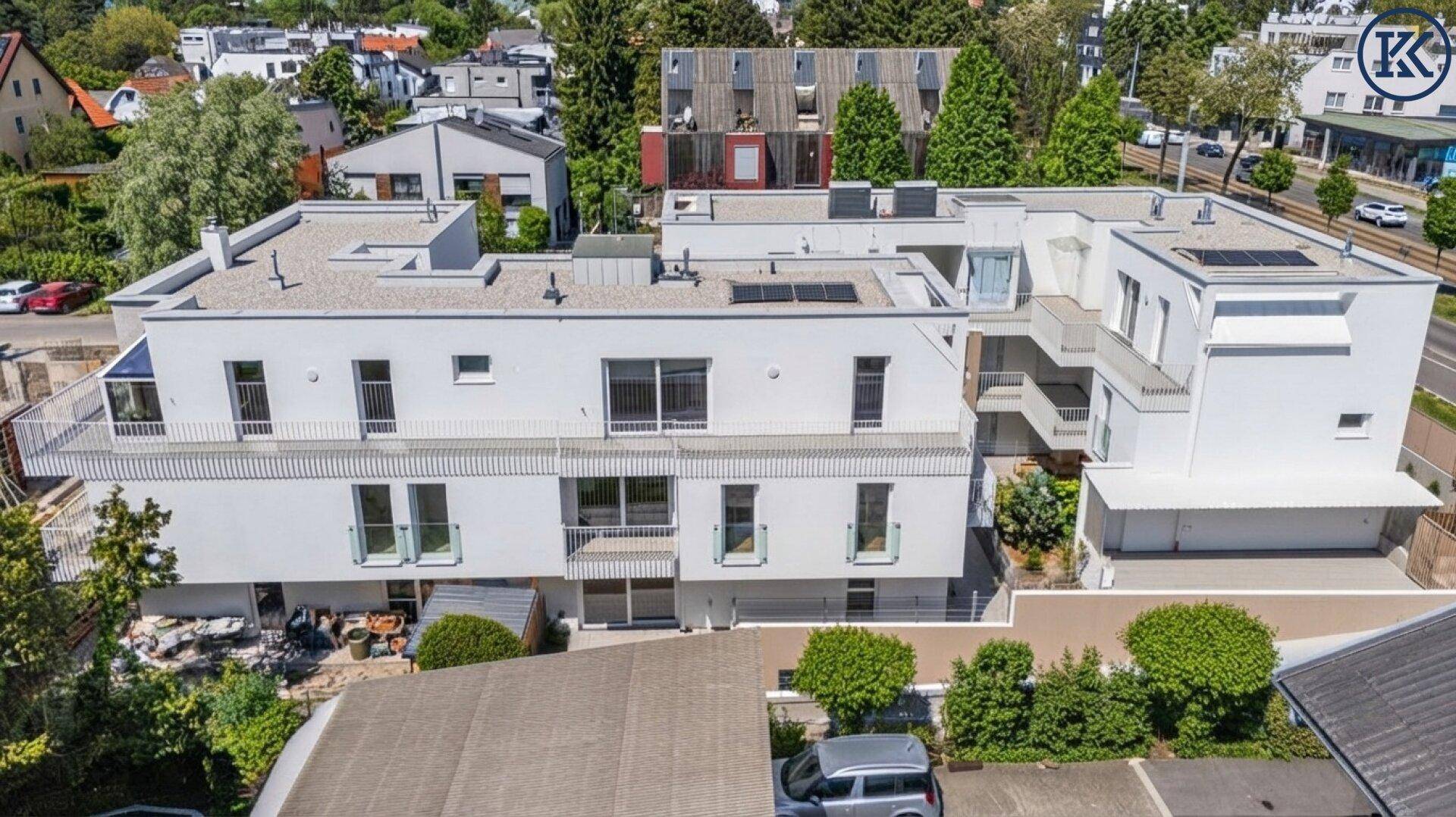 Moderne Wohngebäude mit weißer Fassade, Balkonen und Flachdächern in städtischer Umgebung.