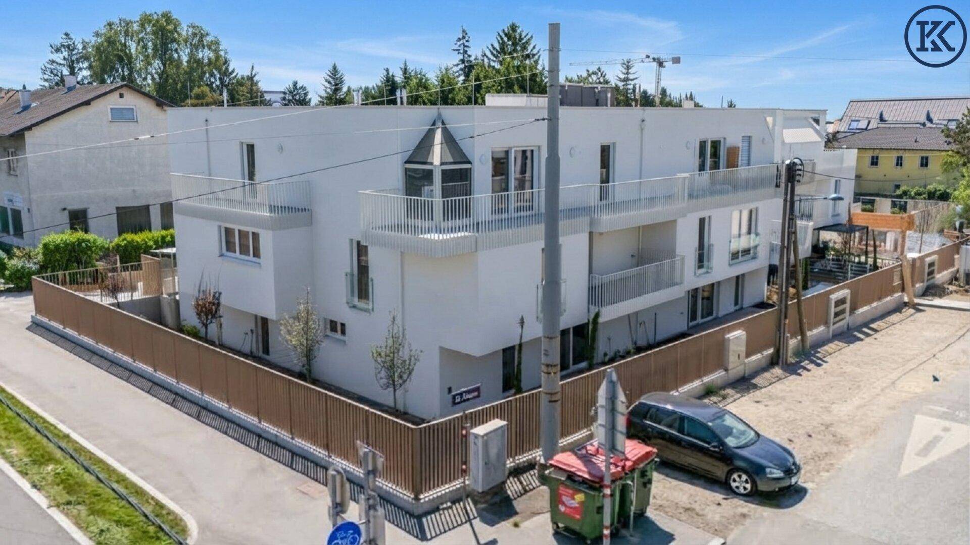 Eckgebäude mit moderner weißer Fassade, Balkonen und einem markanten Erker.