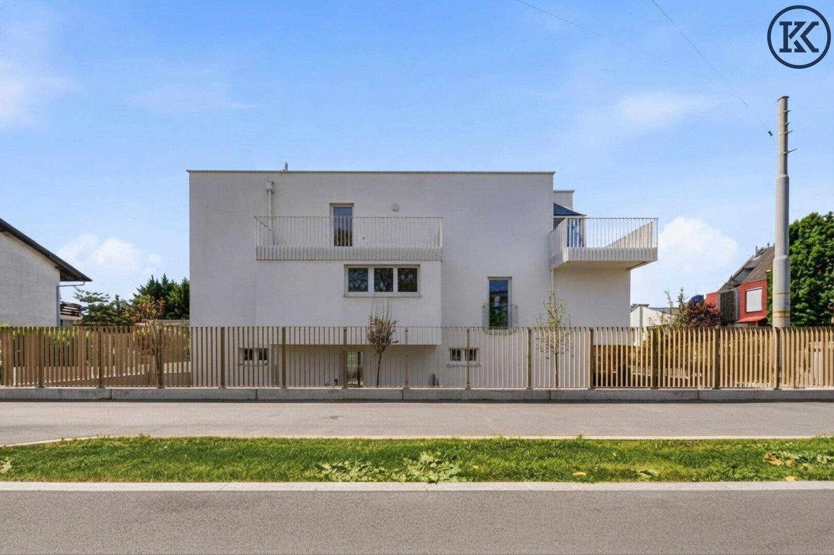 Seitenansicht eines modernen Wohngebäudes mit Balkonen und Holzlattenzaun zur Straße hin.