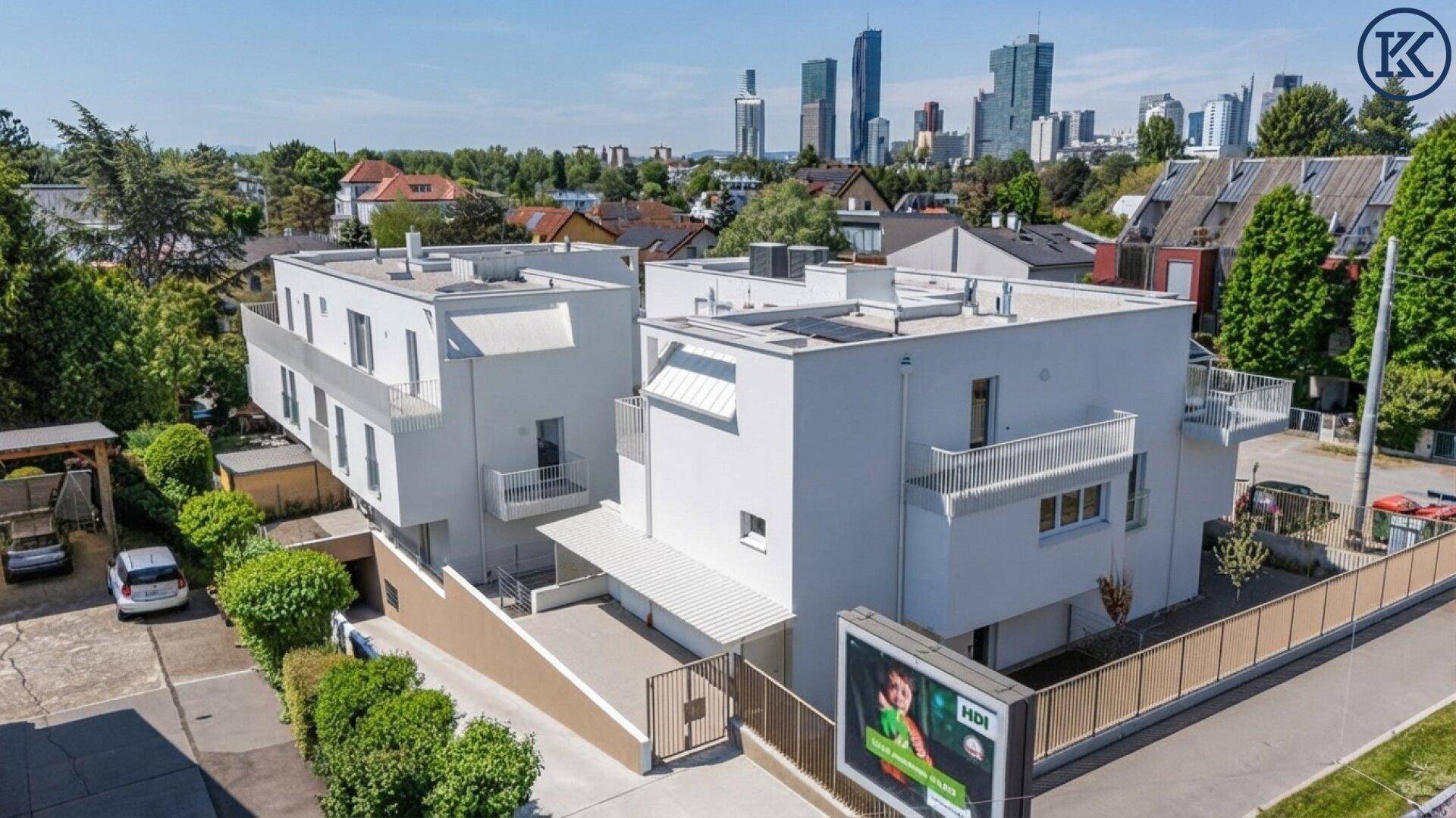 Moderne Wohnanlage von oben mit Tiefgaragenzufahrt und Stadtpanorama im Hintergrund.