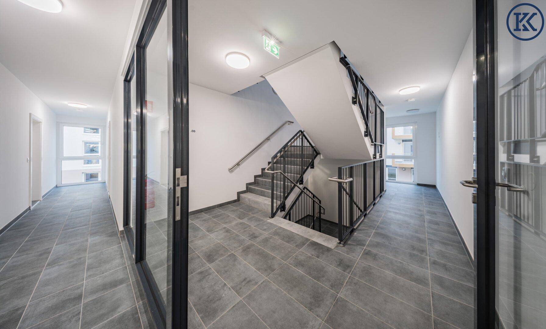 Geräumiger Treppenhausbereich mit Fliesenboden und modernem Geländer in einem Mehrfamilienhaus.