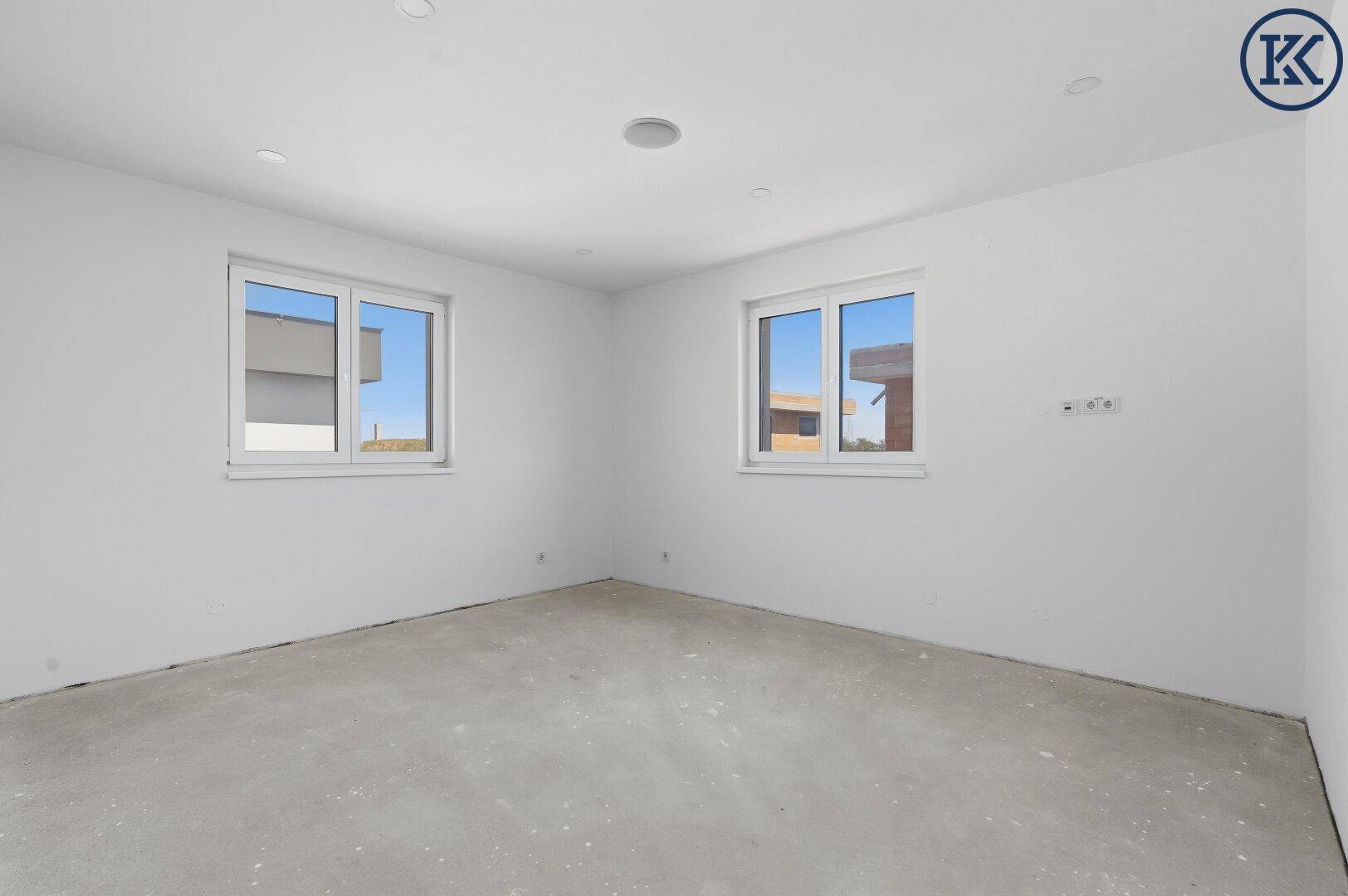 Leeres Zimmer im Rohbau mit zwei Fenstern und vorbereiteten Wänden für den weiteren Ausbau.