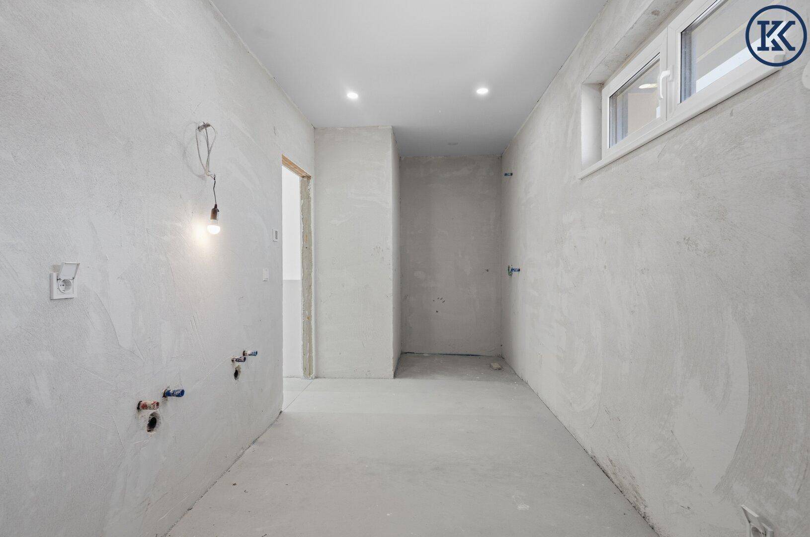 Langer Raum im Rohbau mit Fenster und vorbereiteten Anschlüssen für Sanitärinstallationen.