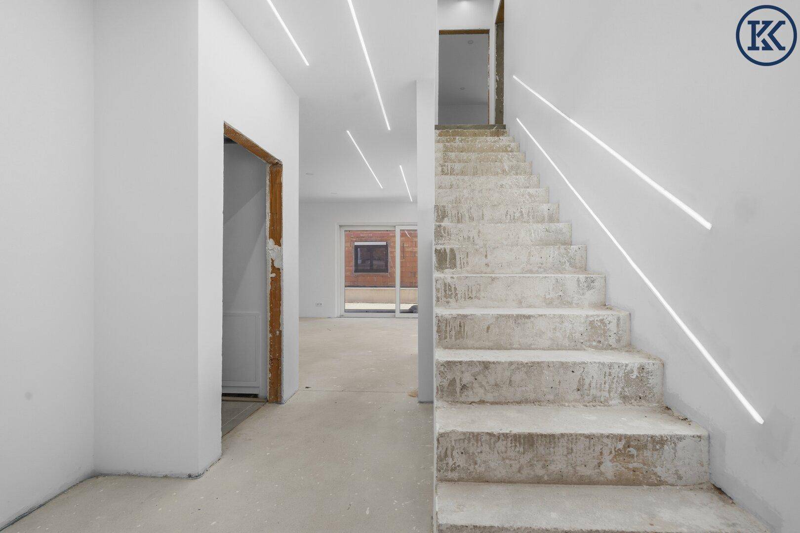 Treppenhaus und Flur im Rohbau mit Betonstufen und modernen Lichtleisten an der Decke.
