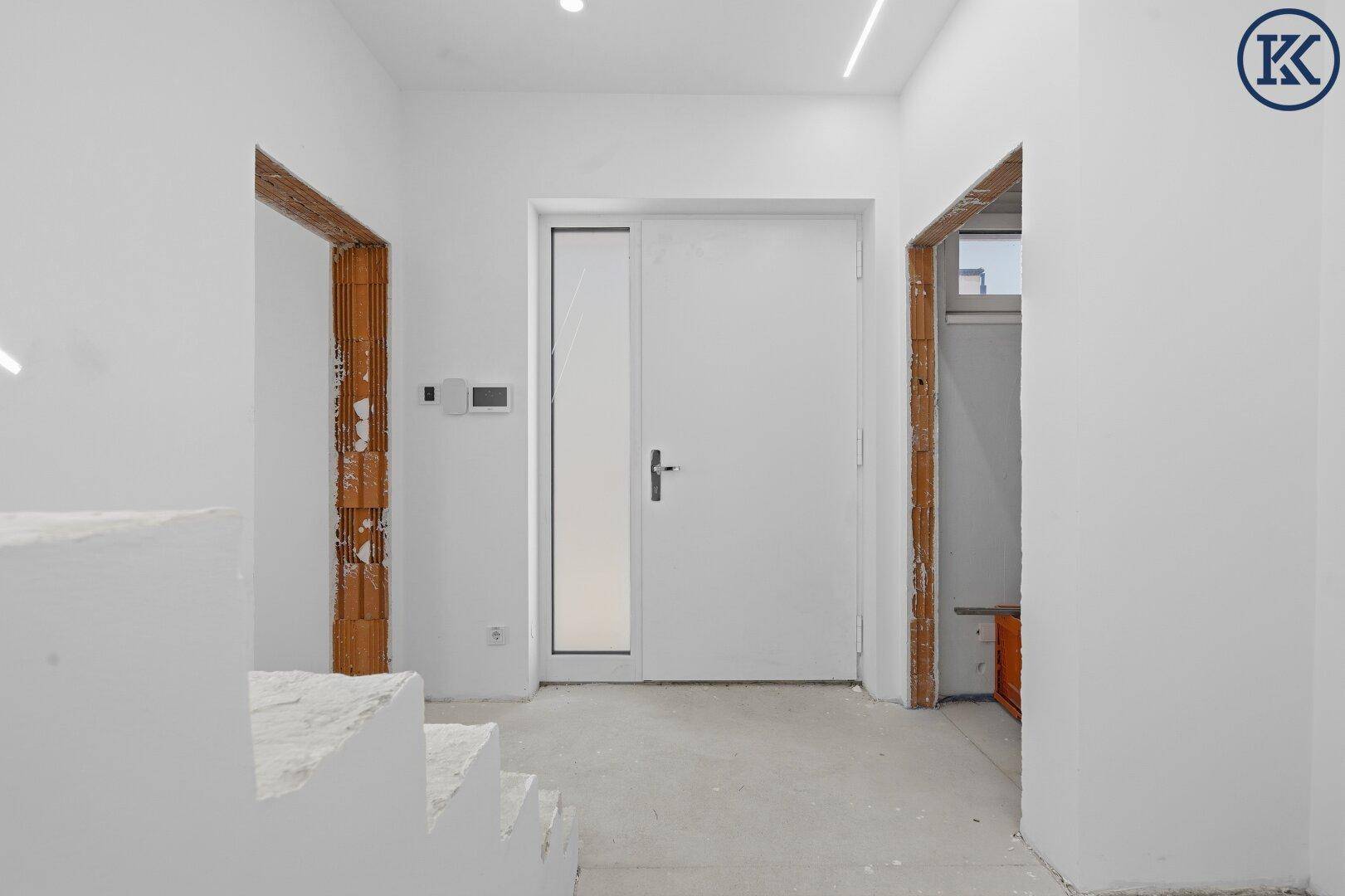 Heller Eingangsbereich im Rohbau mit weißer Tür und vorbereiteten Wandflächen für den weiteren Ausbau.