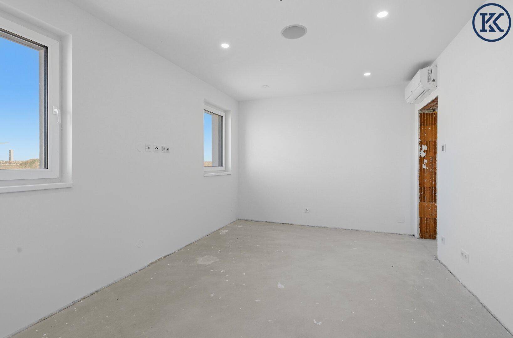 Heller Raum im Rohbau mit zwei Fenstern und vorbereiteten Anschlüssen, bereit für den Innenausbau.