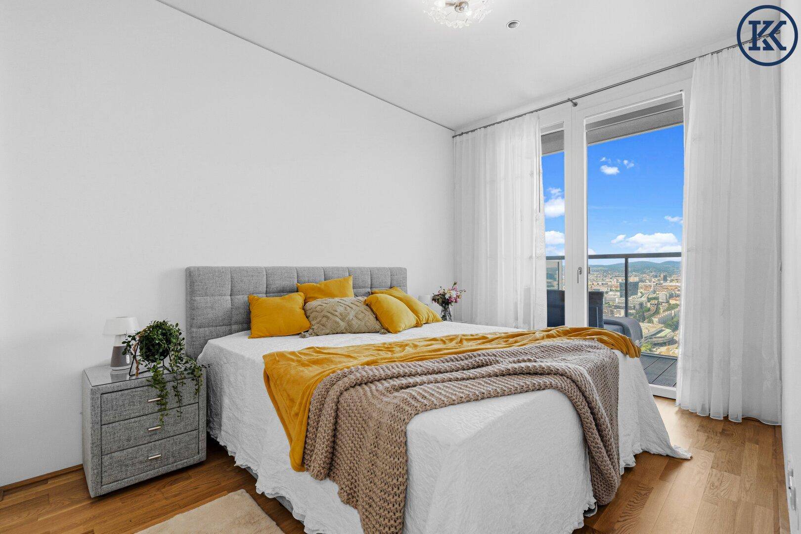 Helles Schlafzimmer mit Doppelbett, Holzboden und Zugang zu einem Balkon mit Aussicht.