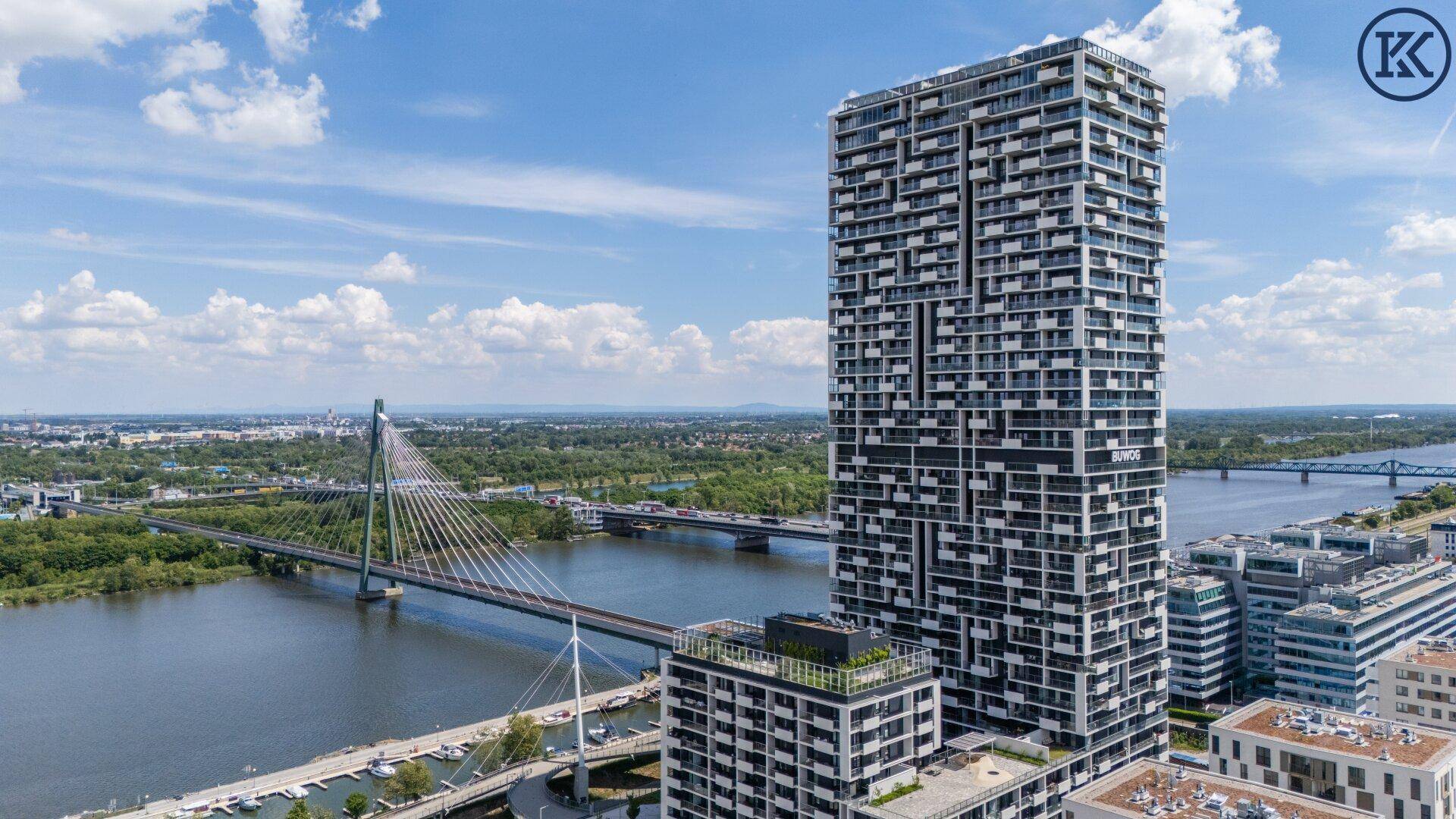 Beeindruckendes Hochhaus mit moderner Architektur und Blick auf die Donau und eine Brücke.