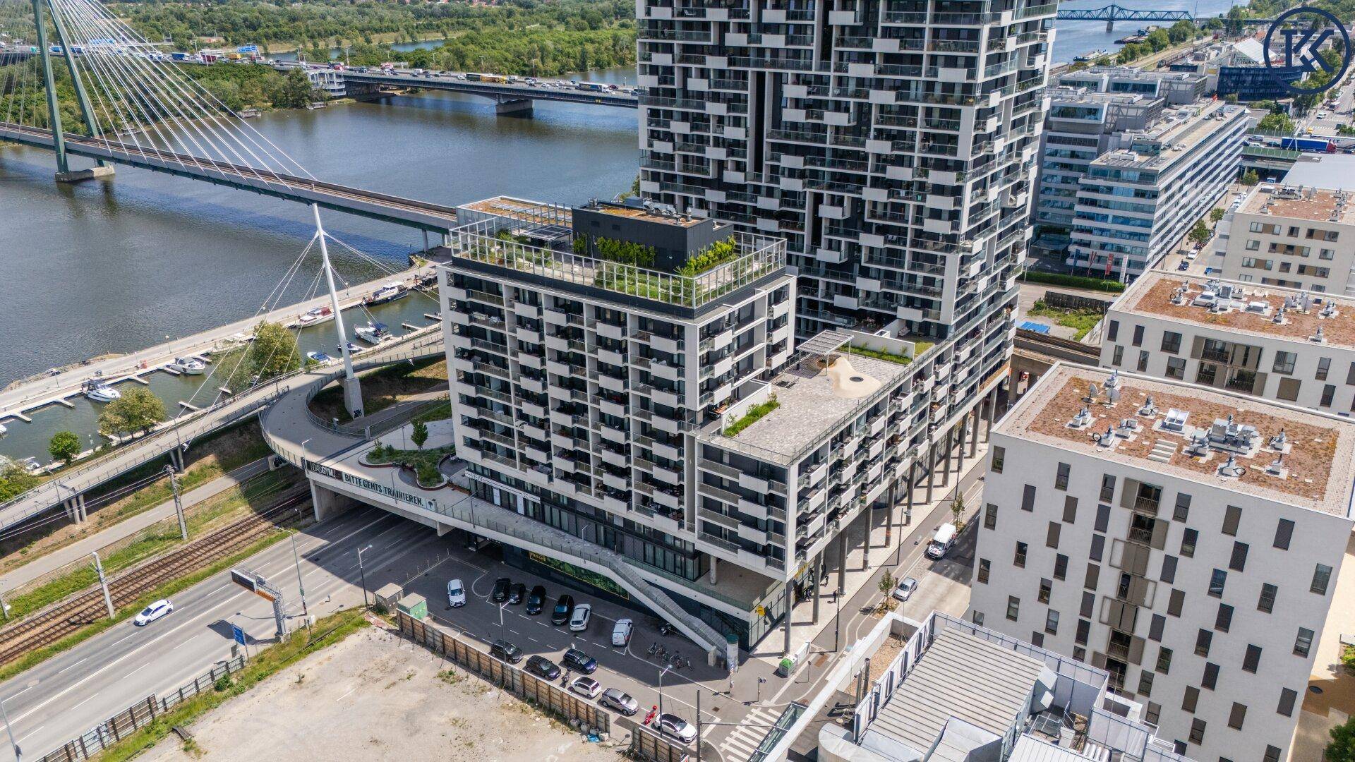 Ansicht eines modernen Hochhauses mit umliegenden Gebäuden und einer Brücke über die Donau.