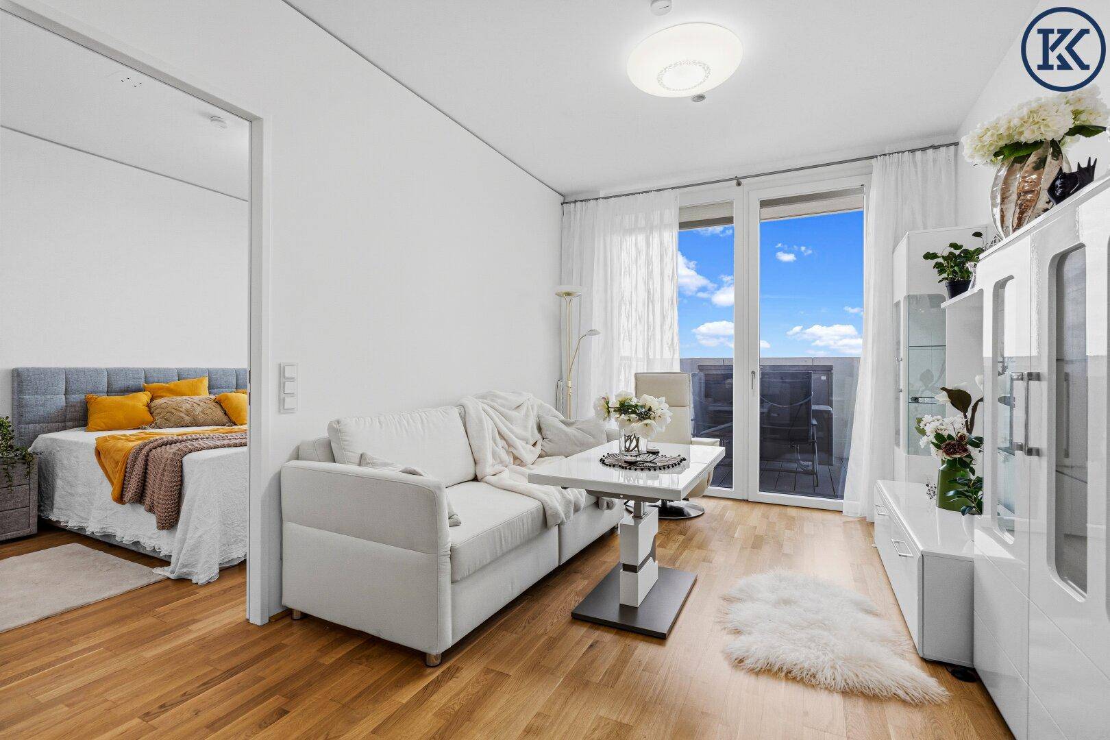 Helles Wohnzimmer mit Holzboden, bequemer Couch und Blick auf das angrenzende Schlafzimmer.