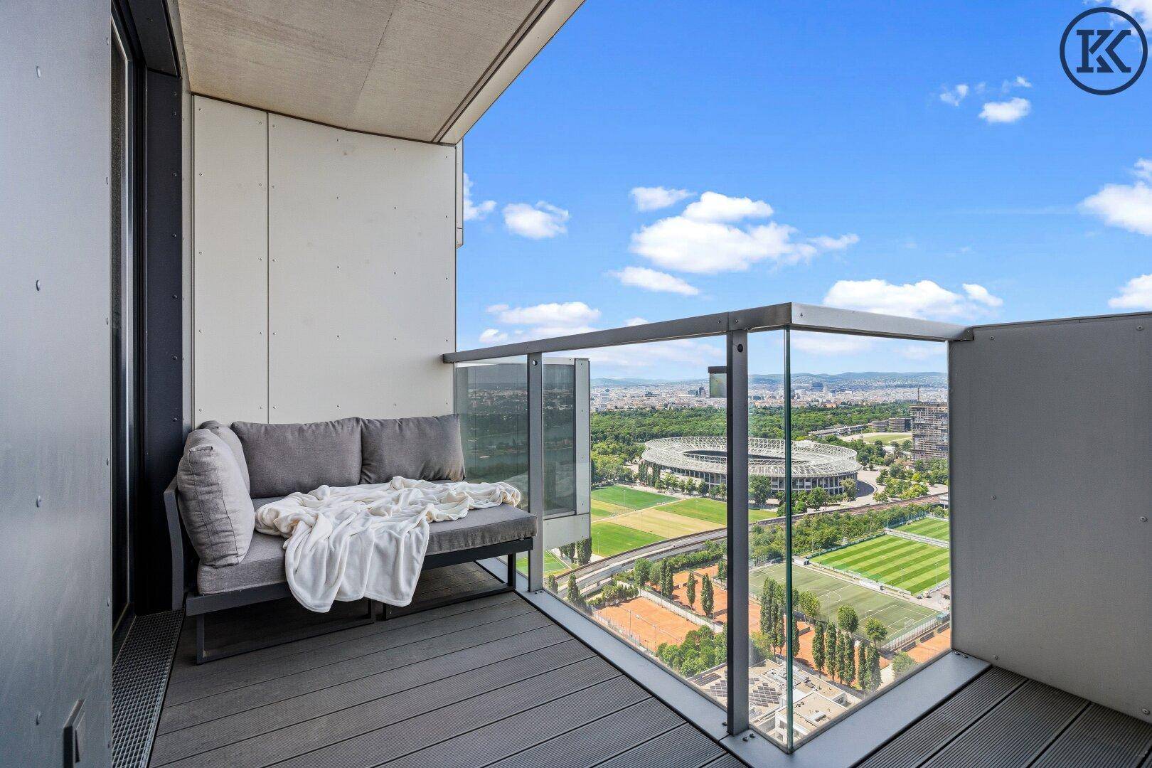 Geräumiger Balkon mit bequemen Outdoor-Möbeln und weitem Blick über die Stadt und Sportanlagen.