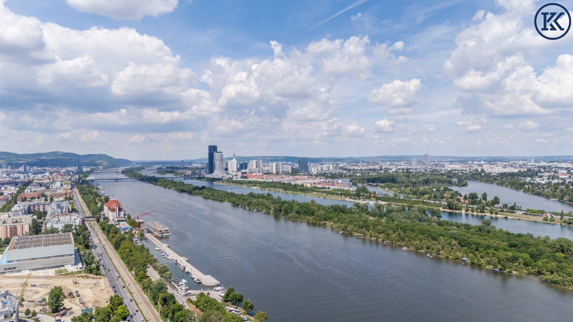 Weitläufiger Panoramablick auf die Donau und die Skyline der Stadt unter blauem Himmel.