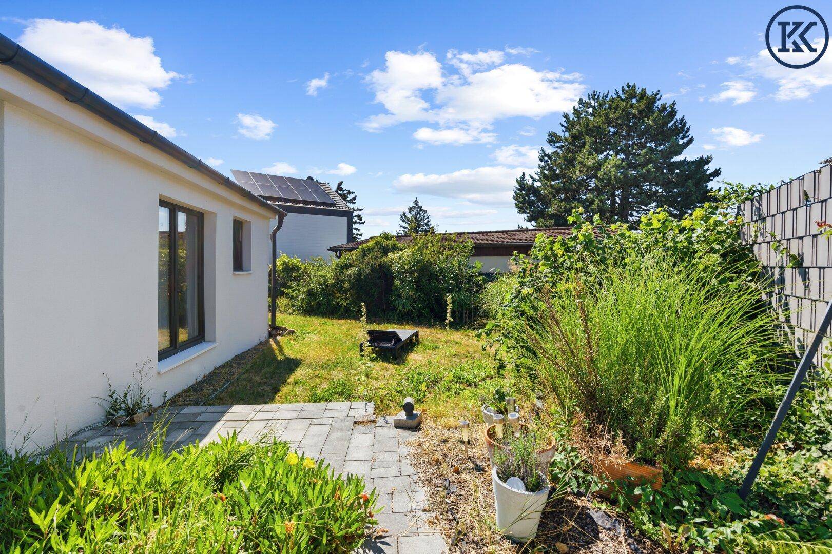 Blick in den grünen Gartenbereich neben dem Haus mit einem gepflasterten Weg und üppiger Vegetation.