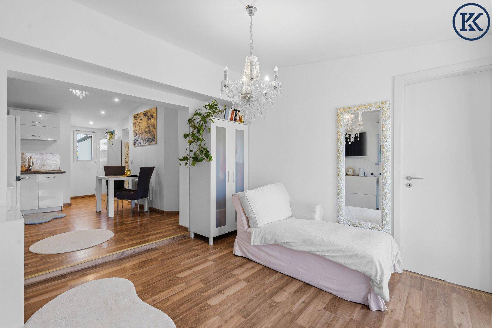 Helles Wohnzimmer mit Holzboden, weißer Einrichtung und einem Kronleuchter, offen zum Essbereich.