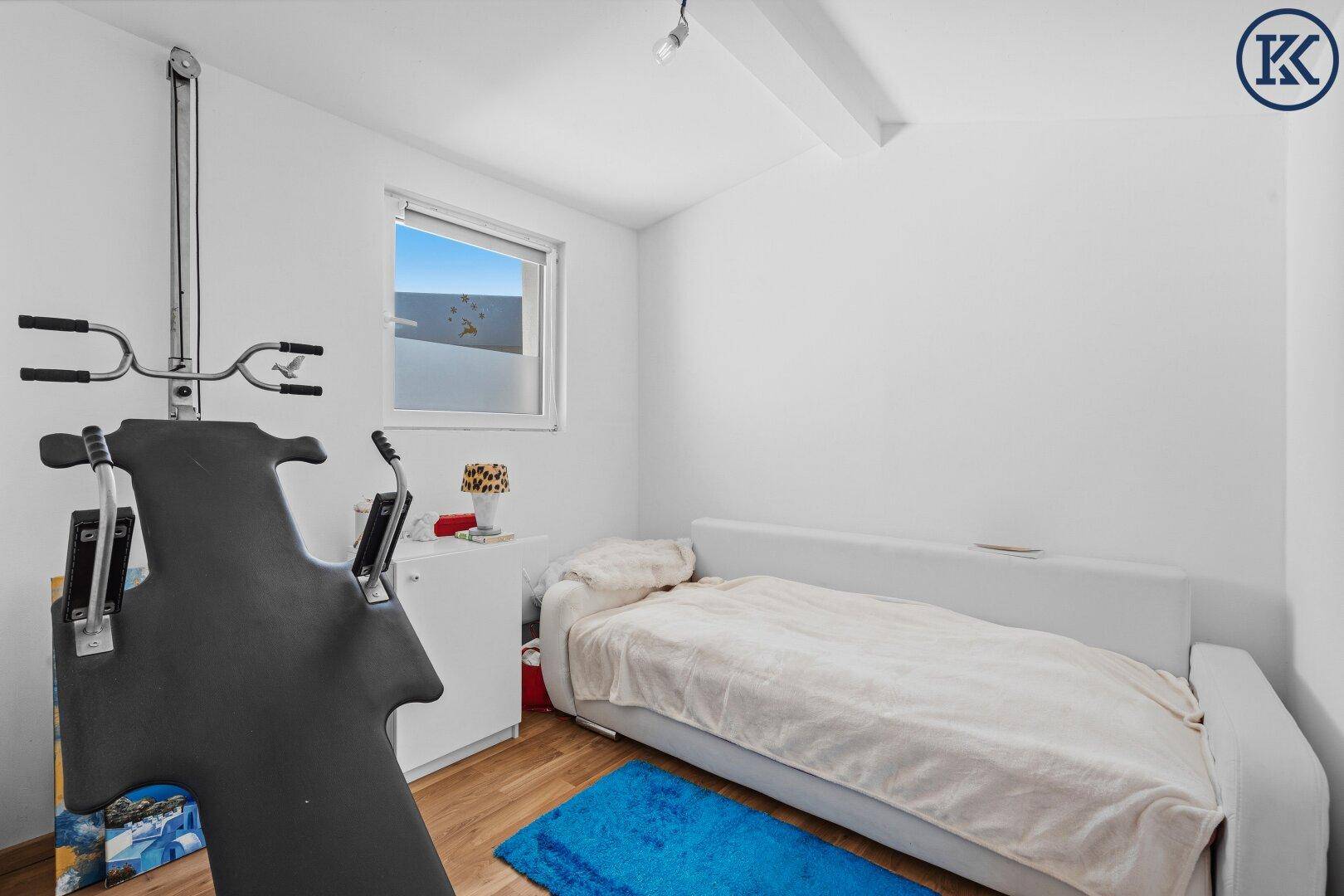Schlafzimmer mit Einzelbett, Holzboden und einem Fitnessgerät, hell und funktional eingerichtet.