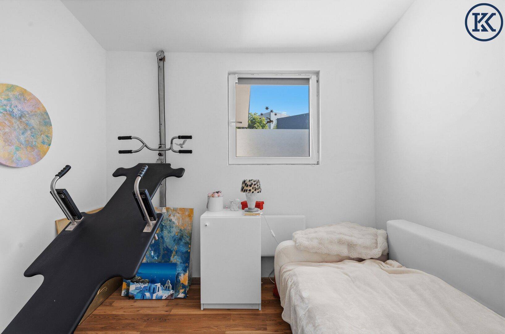Helles Schlafzimmer mit Fitnessgerät, Einzelbett und Fenster, das viel Tageslicht hereinlässt.