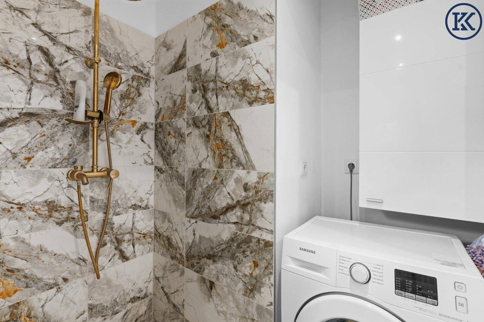 Badezimmer mit begehbarer Dusche, goldenen Armaturen und einer Waschmaschine, praktisch und stilvoll.